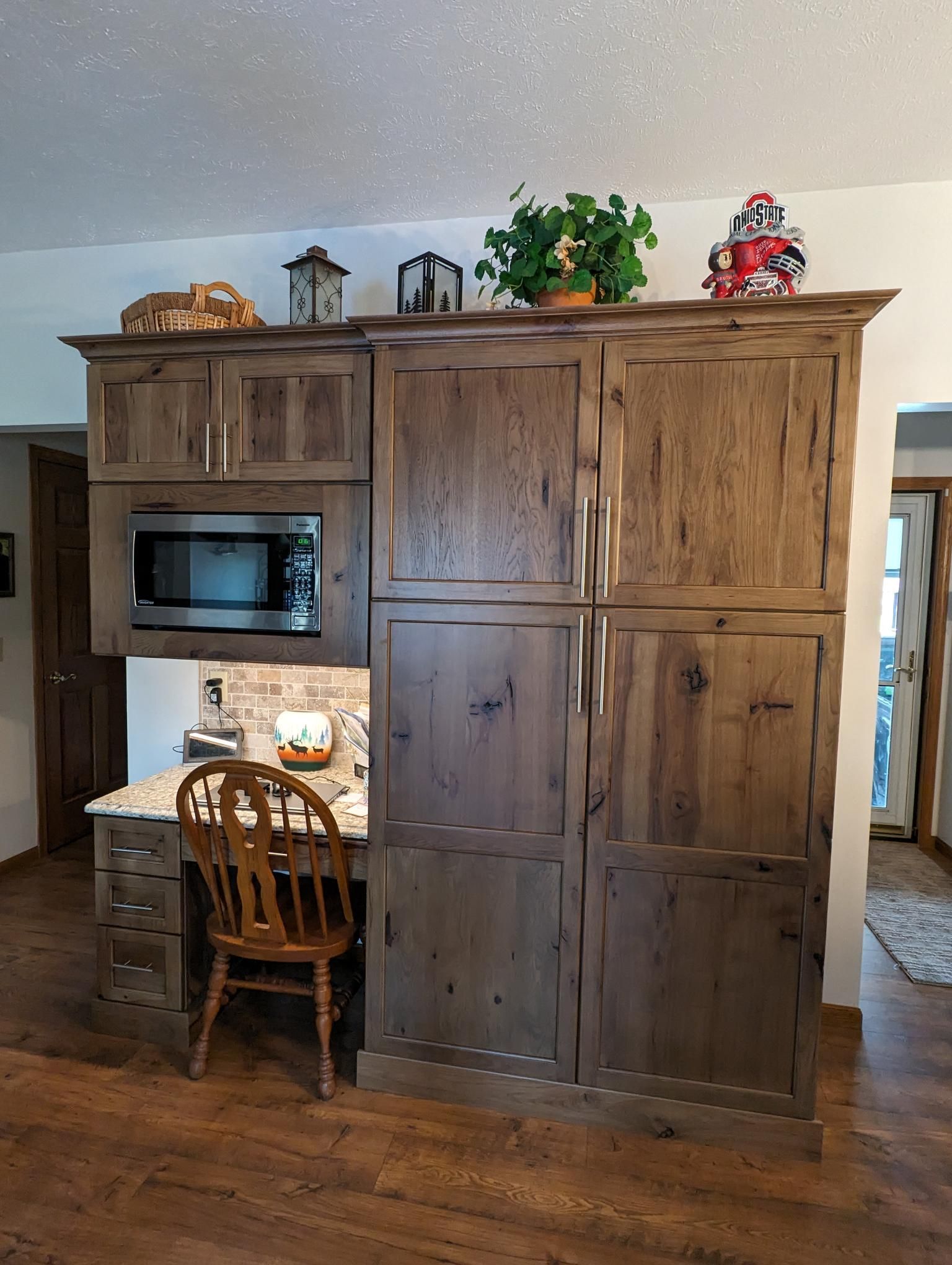 Wooden kitchen cabinetry with a desk and microwave. A chair is positioned at the desk.