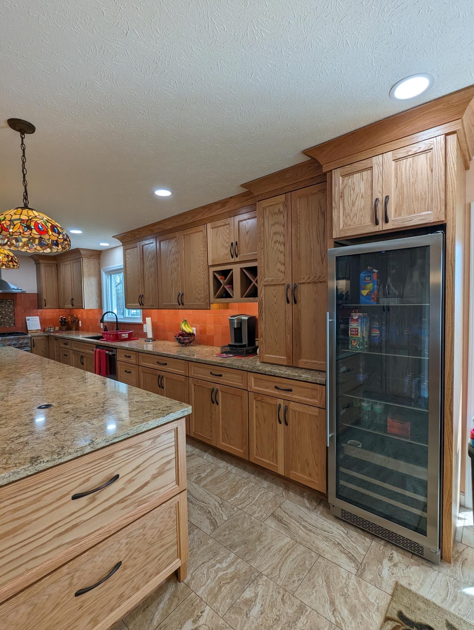A kitchen with wood cabinets, granite countertops, and a wine fridge.