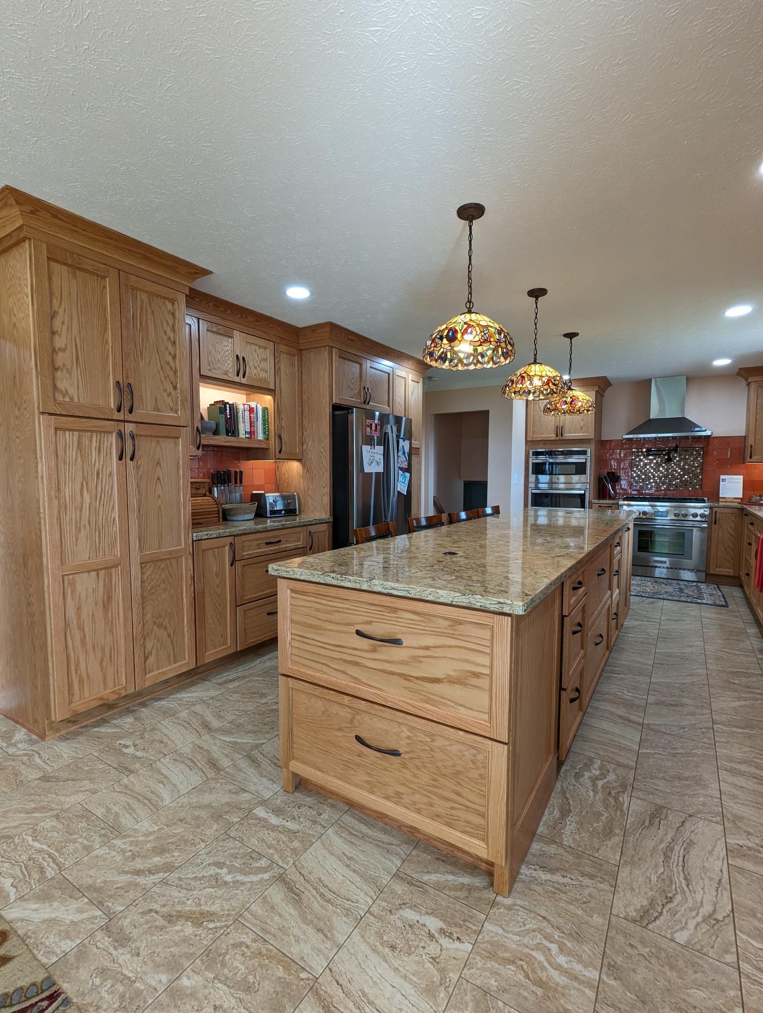 Kitchen with wood cabinets, granite countertops, and a large island with hanging lights.