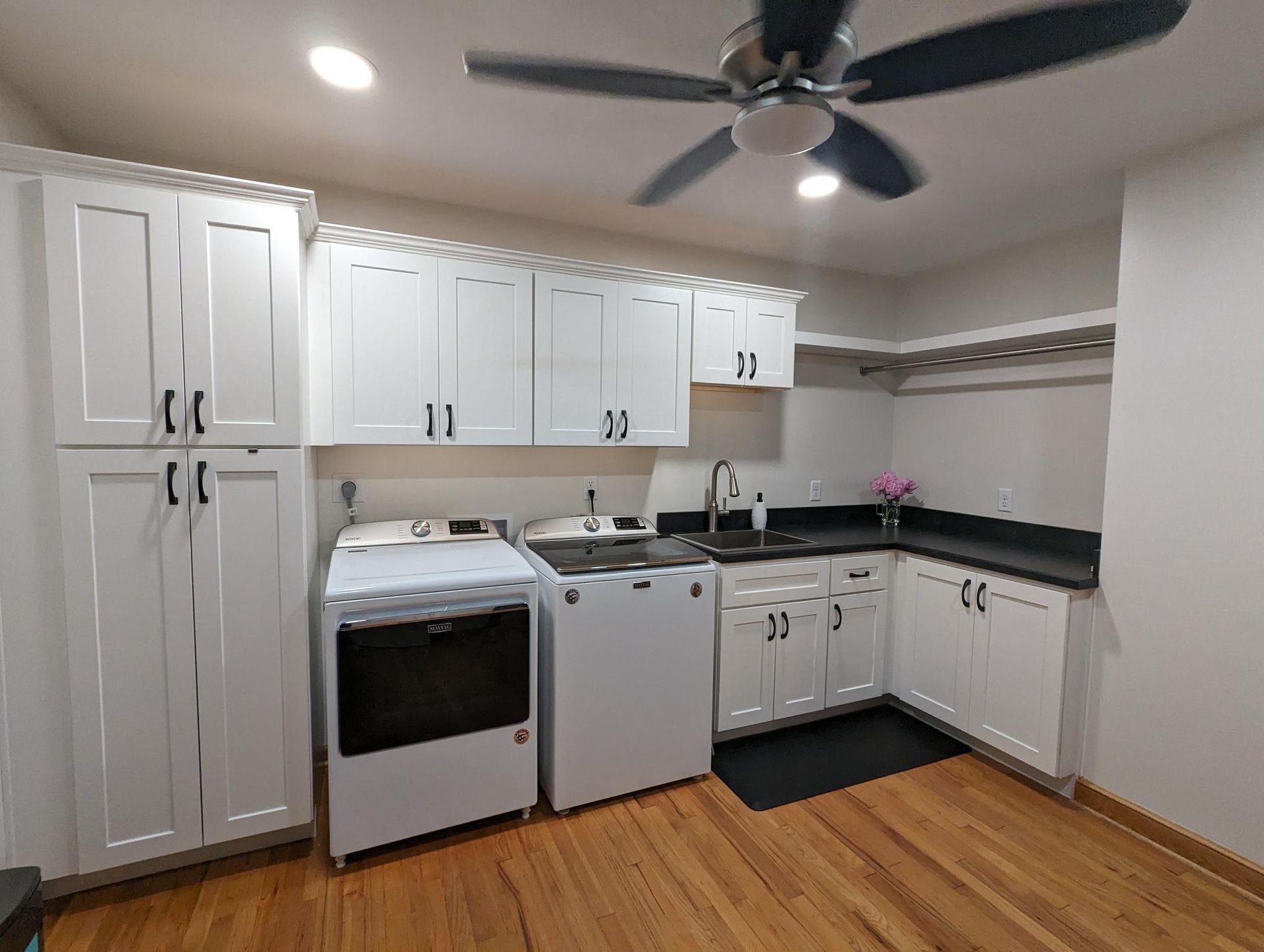 Laundry room with white cabinets, black countertops, washer, dryer, and hardwood floors.