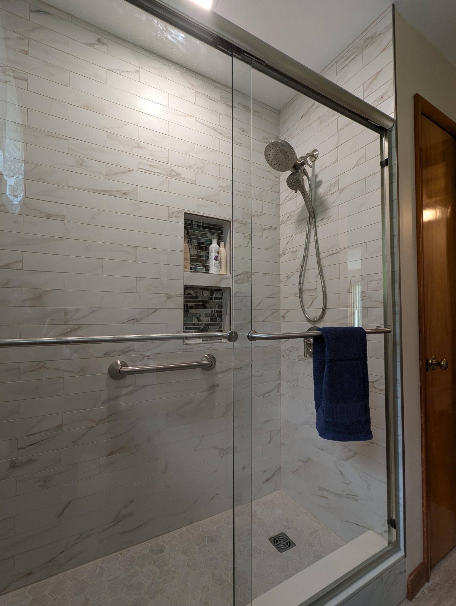 Shower with glass doors, white tile walls, and a recessed shelf. A blue towel hangs inside.