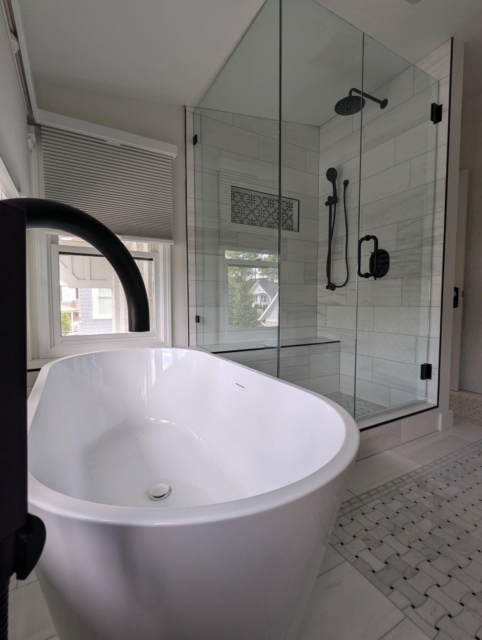 White freestanding bathtub and glass shower in a modern bathroom with black fixtures.