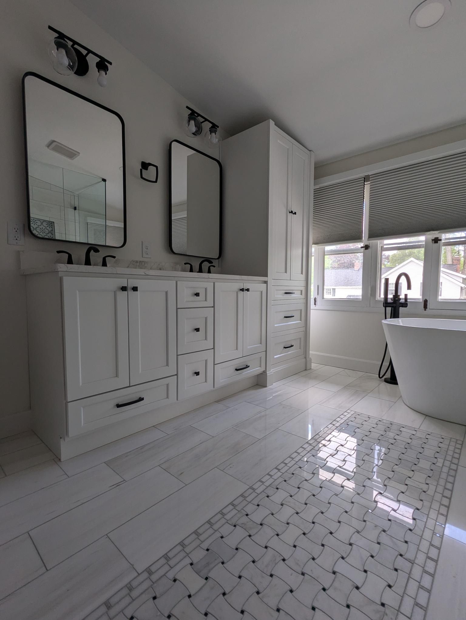 White bathroom with double vanity, tall cabinet, bathtub, and patterned floor.