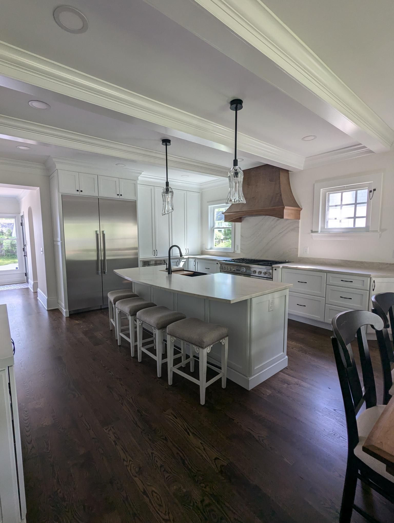 Modern kitchen with white cabinets, island, stainless steel appliances, dark wood floor, and pendant lights.