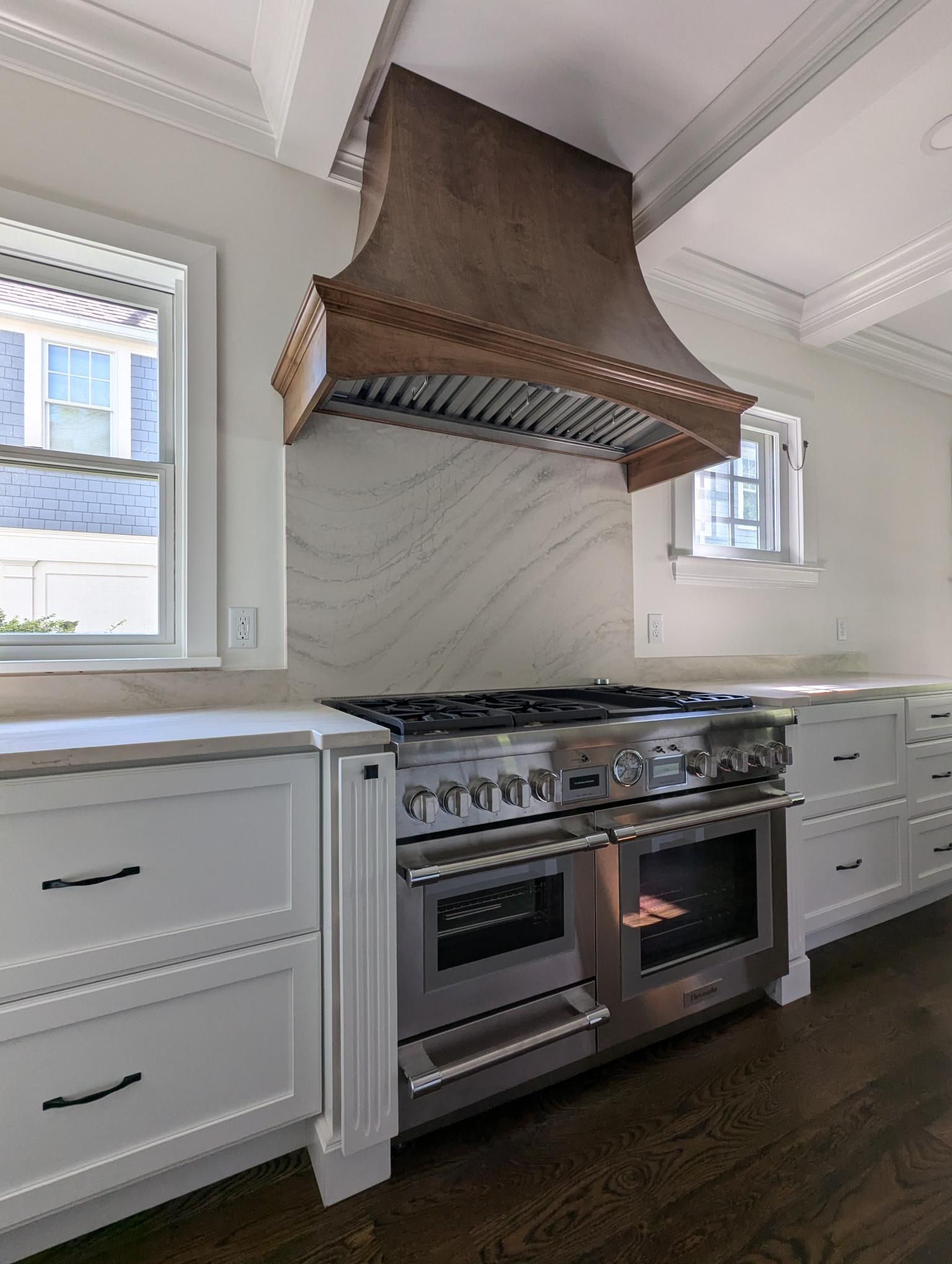 Stainless steel range and hood in white kitchen with marble backsplash.