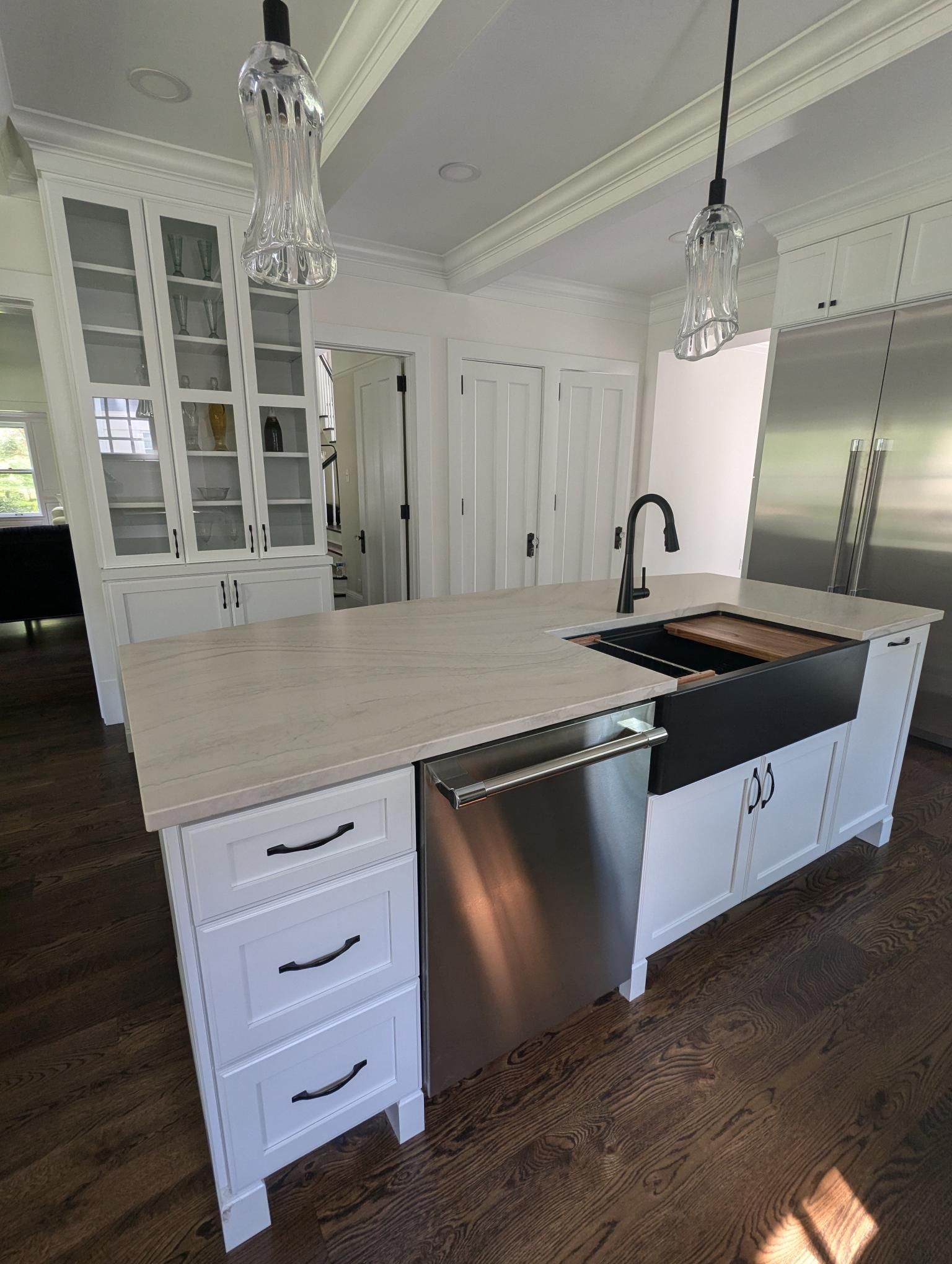 White kitchen island with a stainless steel dishwasher and black sink, dark wood floors.