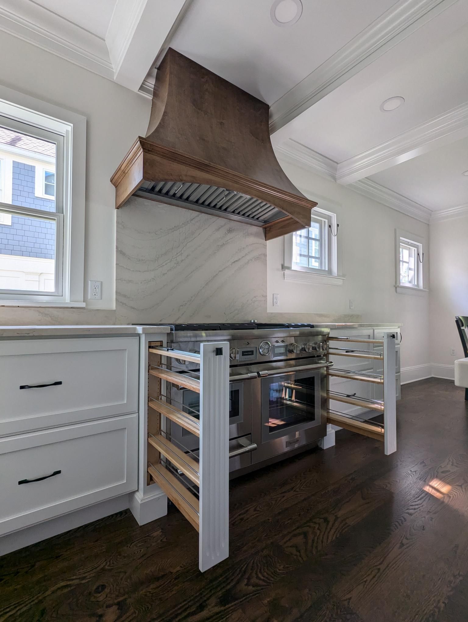Kitchen with stainless steel stove, wooden hood, white cabinets, and wine racks. Dark wood floor.