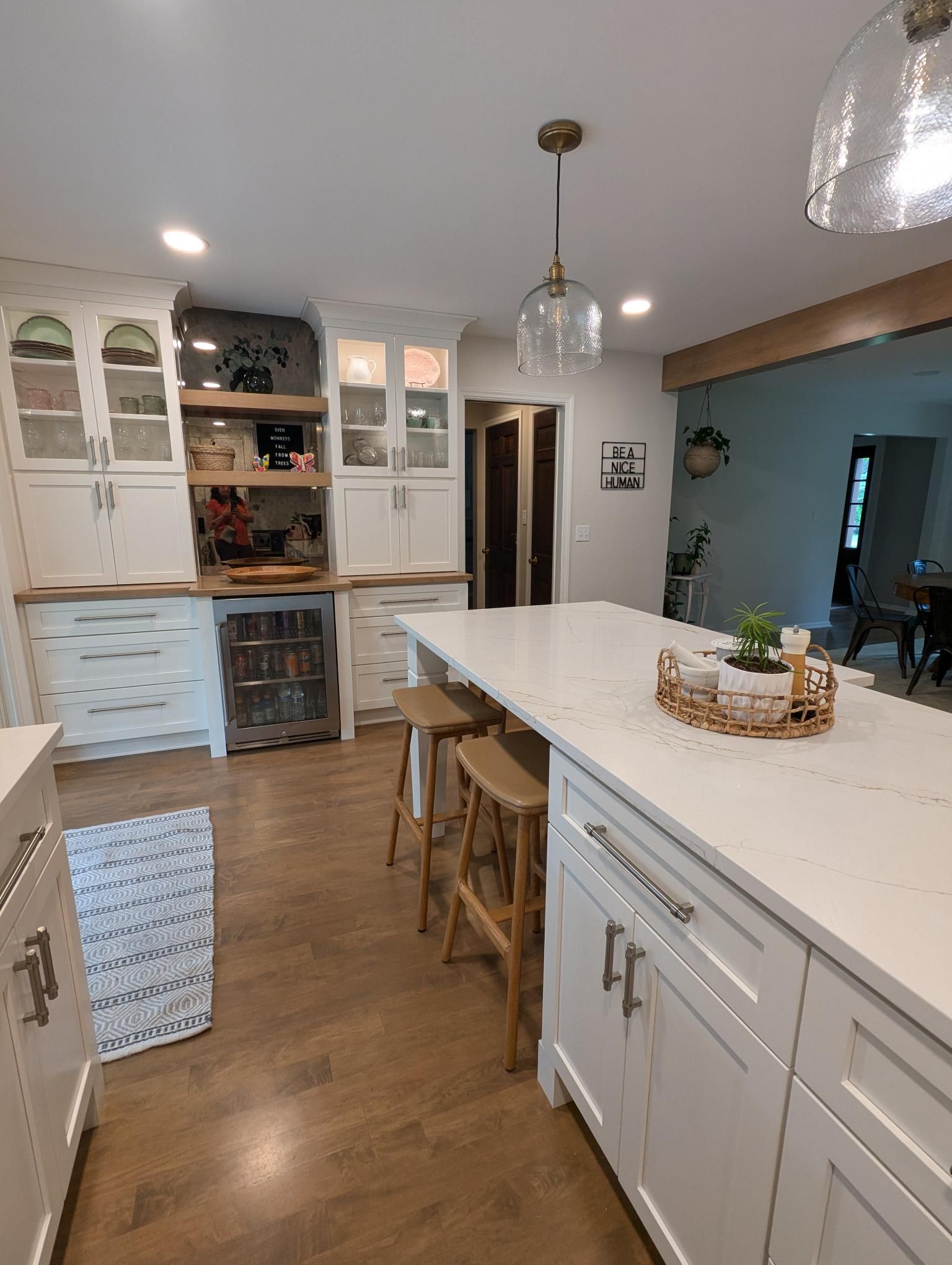 Modern white kitchen with island, wooden stools, and glass pendant light.