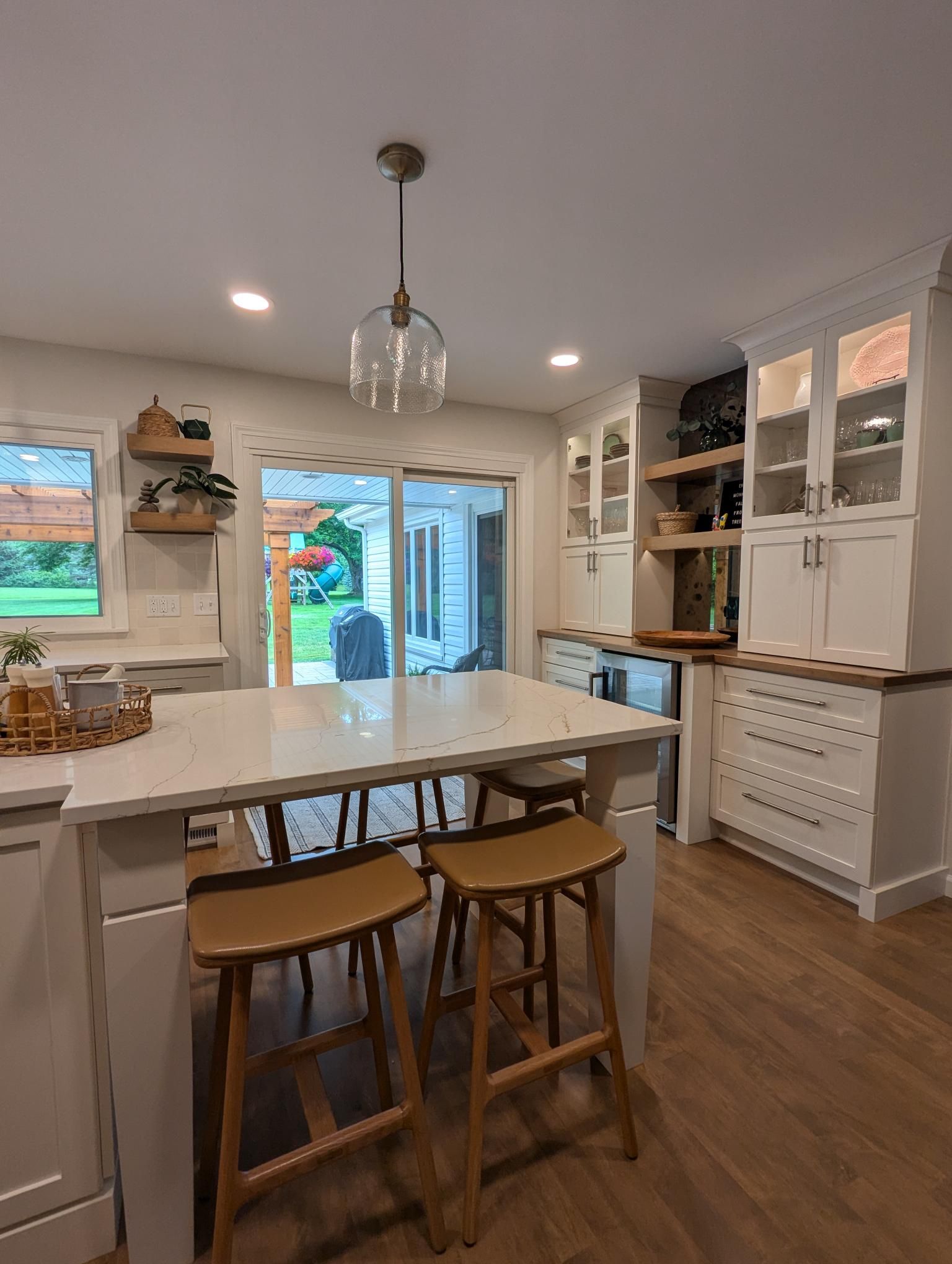 Kitchen with island, light wood floors, white cabinets, and outdoor view through sliding glass door.