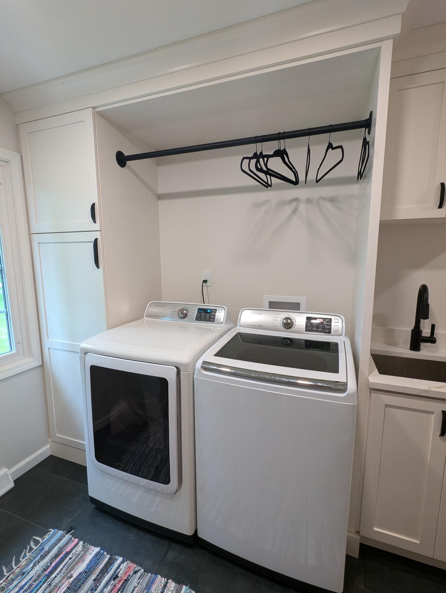 Laundry room with white appliances, hanging rod, and cabinetry.