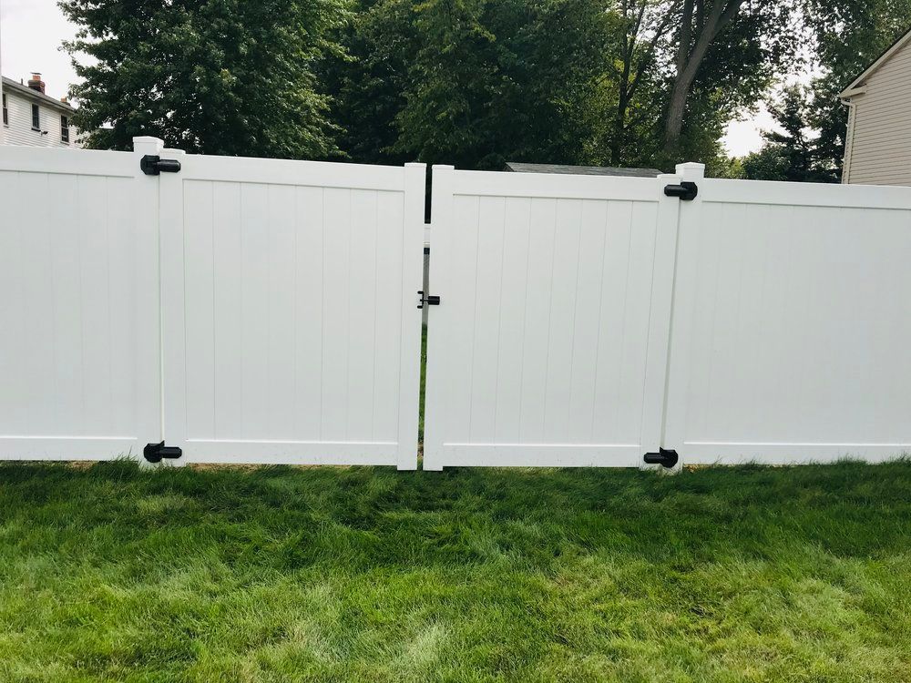 White vinyl fence with a double gate in a grassy yard.