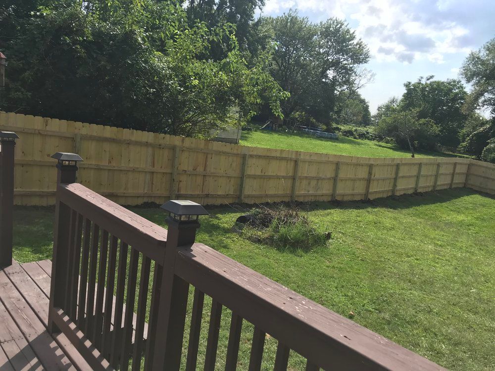 Wooden fence curving through a grassy yard, viewed from a wooden deck with a railing.