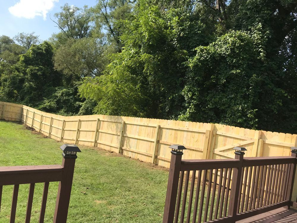 Wooden fence in a backyard, with a deck in the foreground and trees in the background.