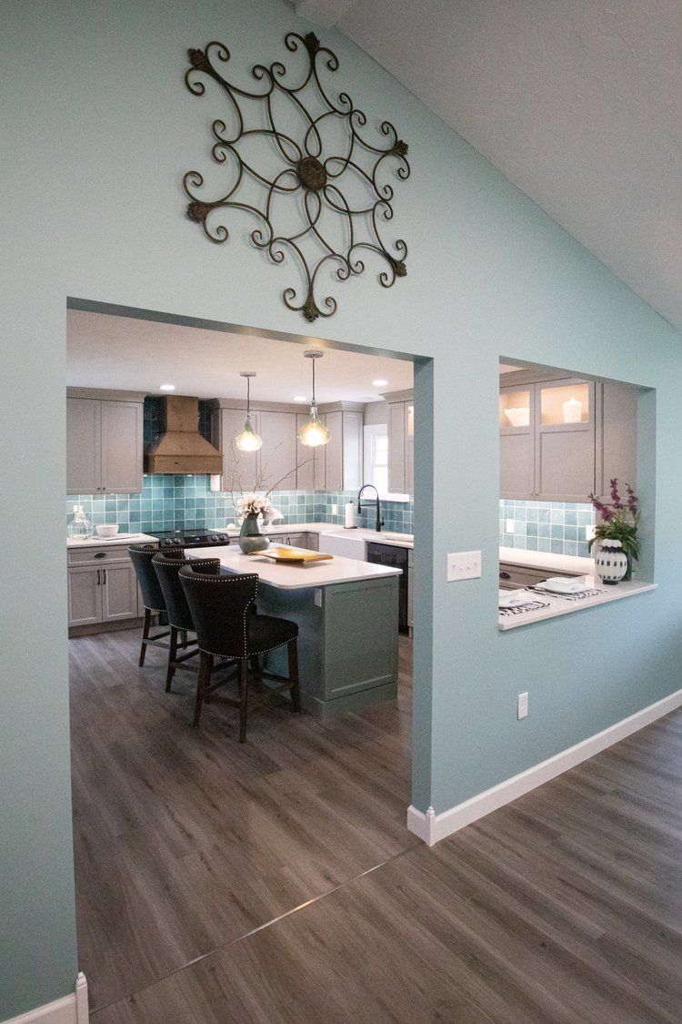 Interior with kitchen visible through doorway, light blue walls, gray wood-look floors, decorative metal wall art.