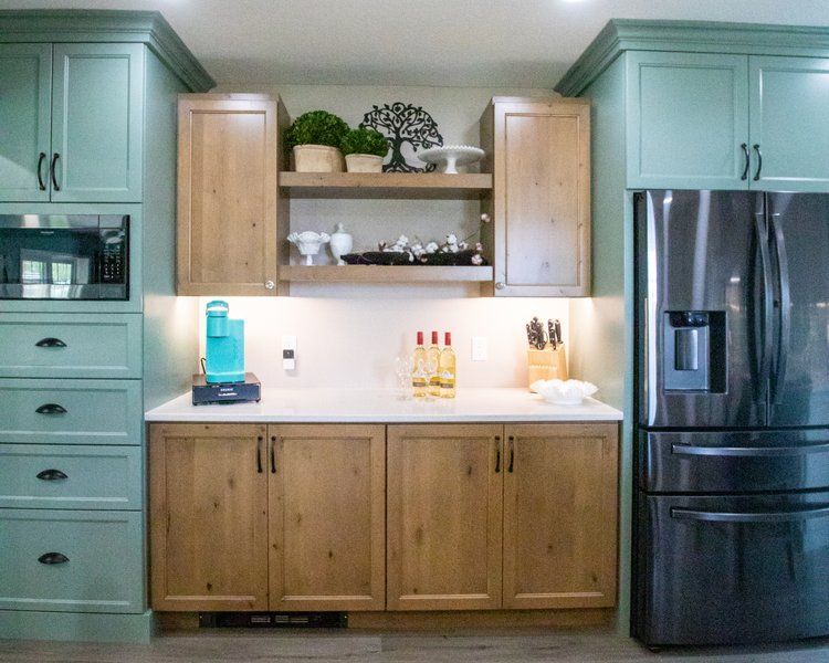 Kitchen with teal and wood cabinets, a stainless steel refrigerator, and a white countertop.
