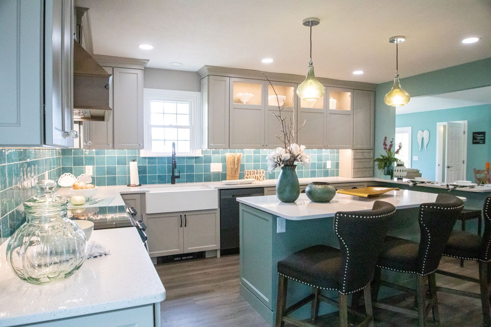 Kitchen with light blue cabinets, turquoise backsplash, and white countertops. Island with seating and two pendant lights.