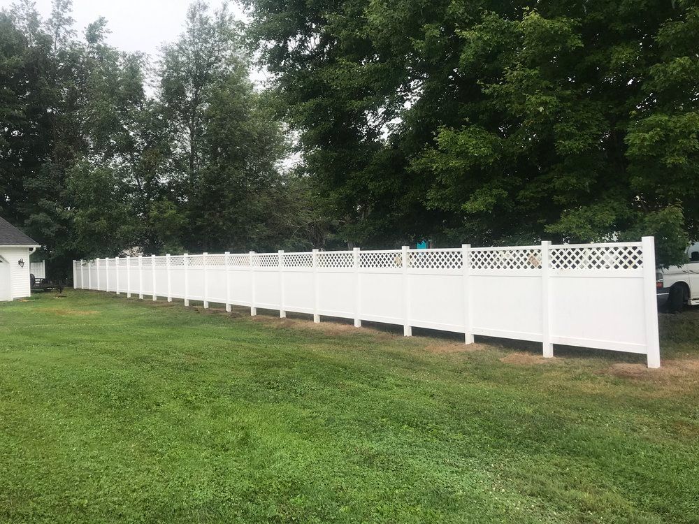 White vinyl fence in a grassy yard, with decorative lattice sections against a backdrop of trees.