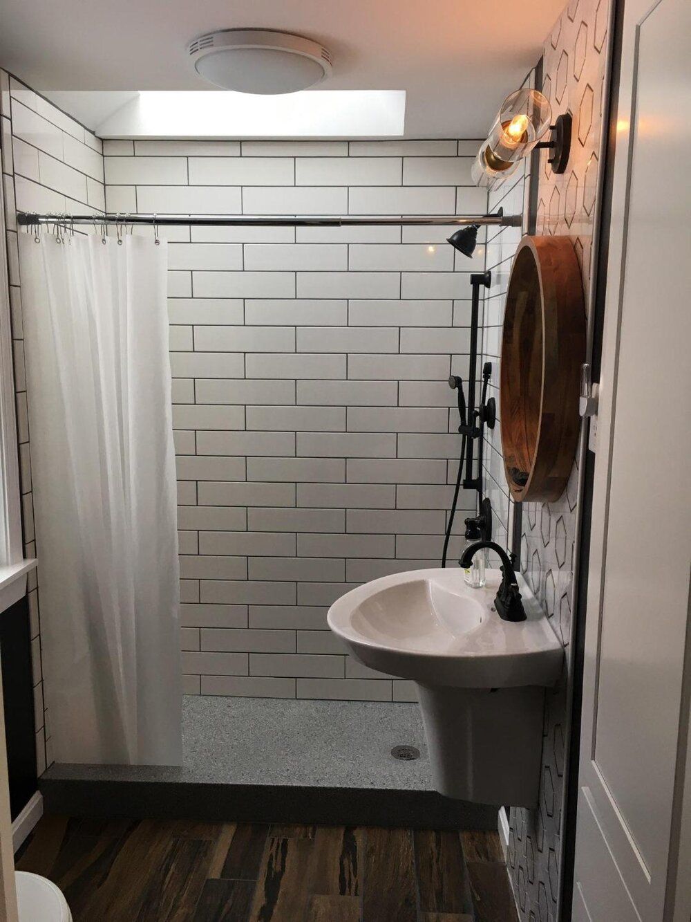 Small bathroom with a white tiled shower, pedestal sink, and a copper mirror.