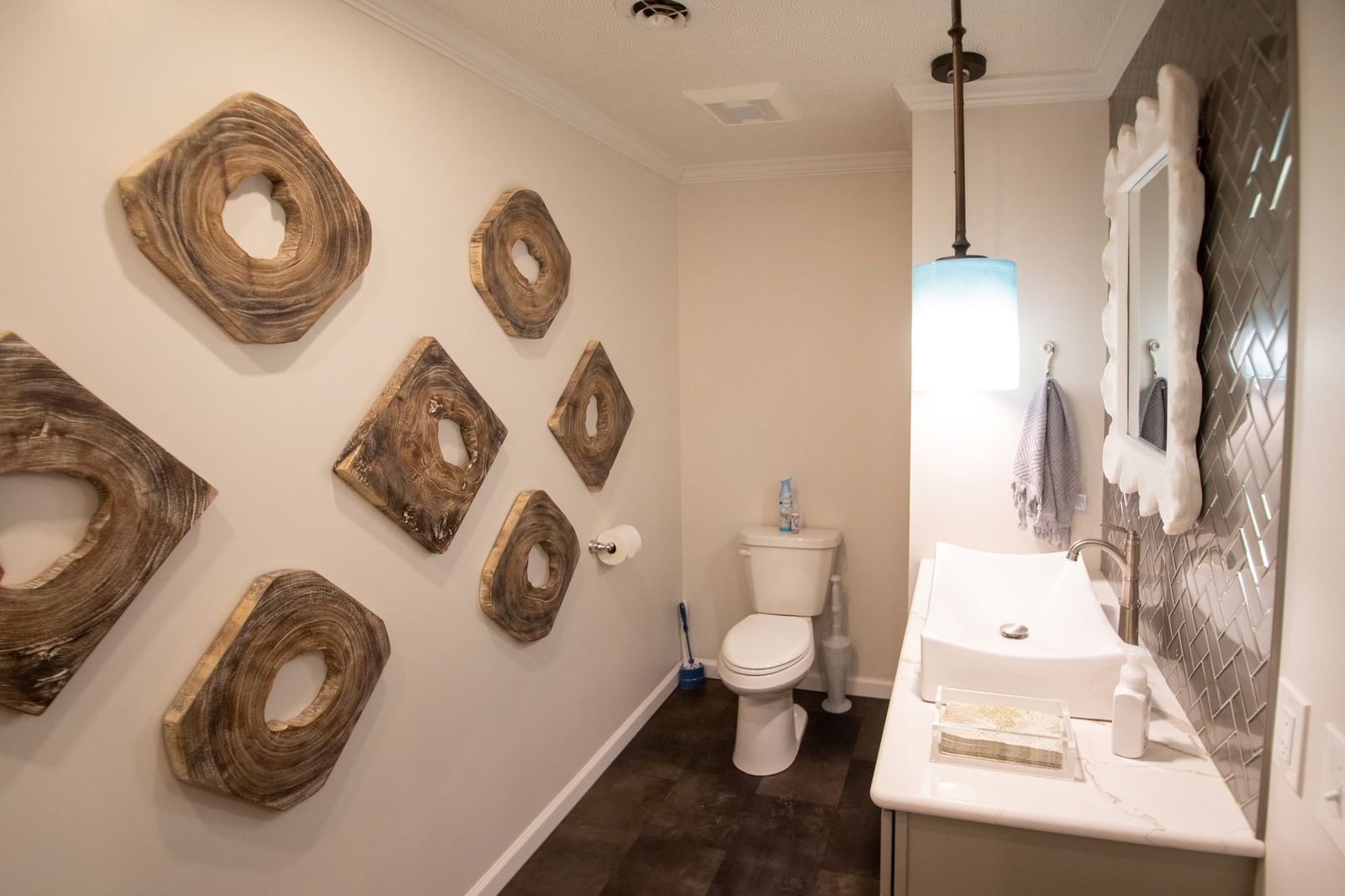 A modern bathroom with wooden wall art, a toilet, a sink, and a patterned metallic accent wall.