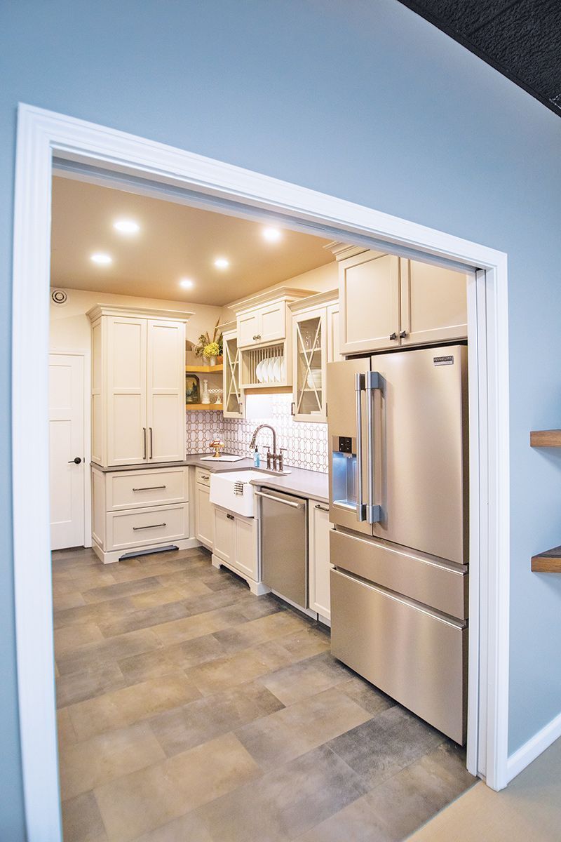 Kitchen framed by a doorway, with stainless steel fridge, light cabinets, and farmhouse sink.