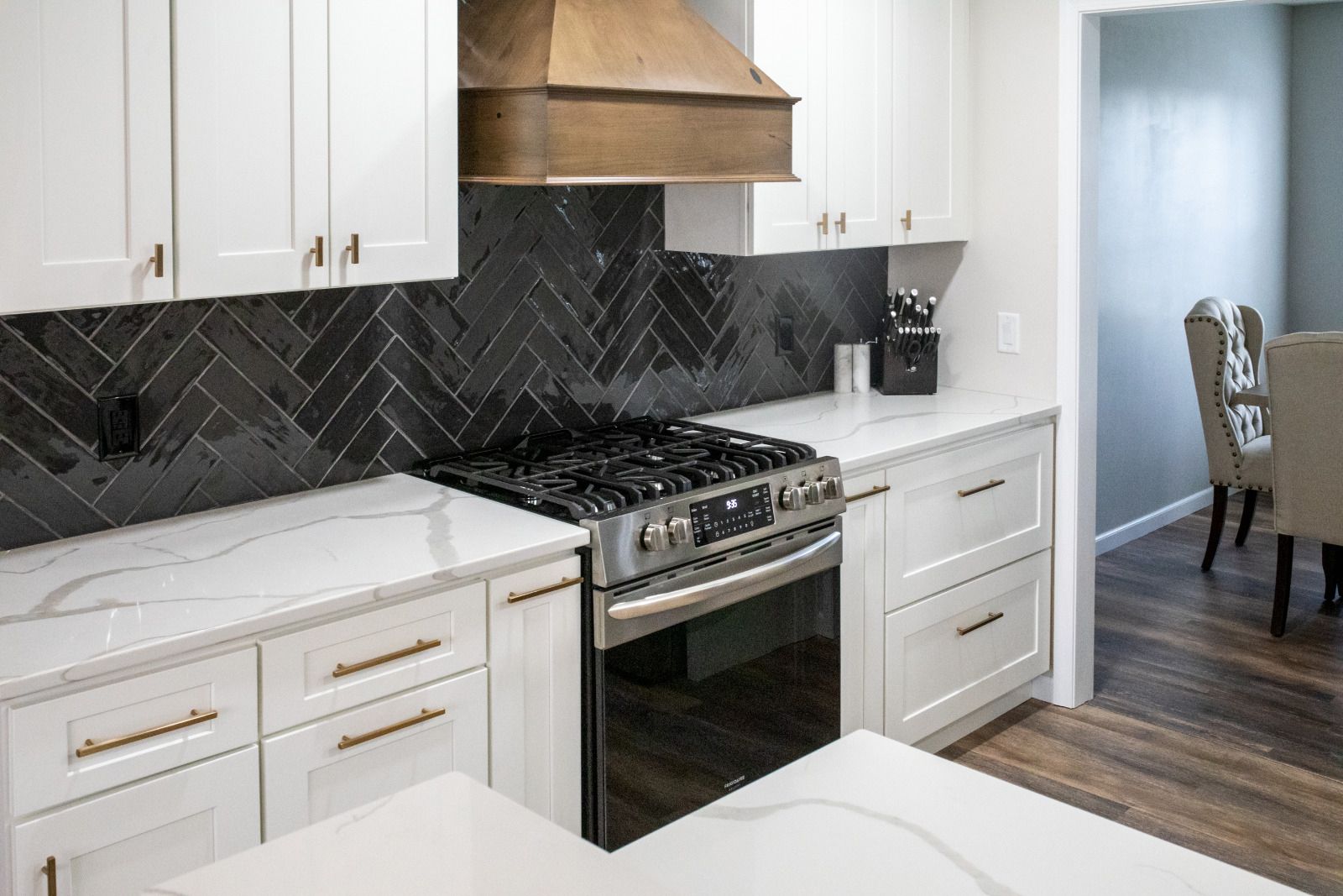 Modern kitchen with white cabinets, dark tile backsplash, stainless steel appliances, and copper range hood.