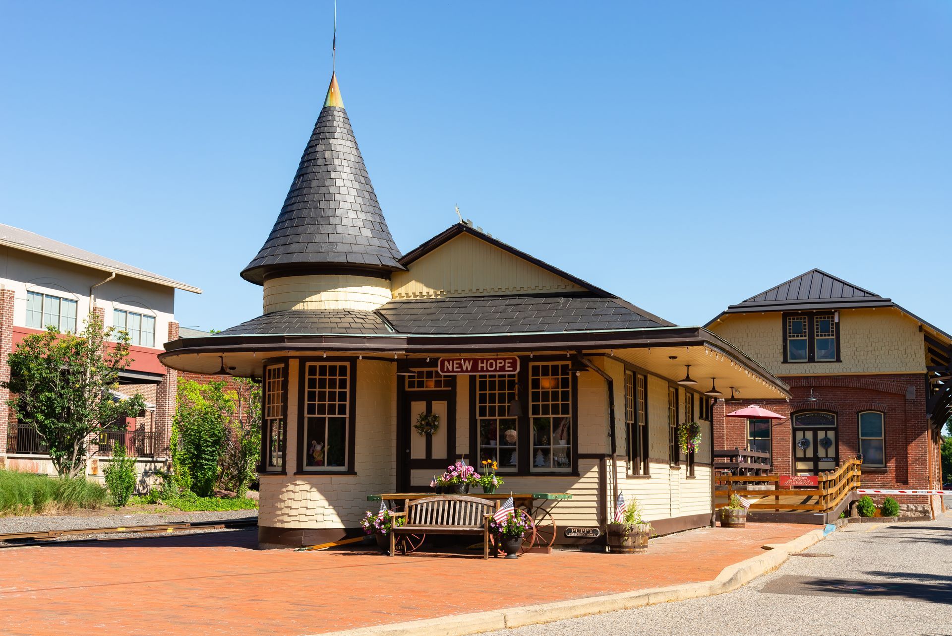 Small brick building with a conical turret and porch in a sunny courtyard under a blue sky