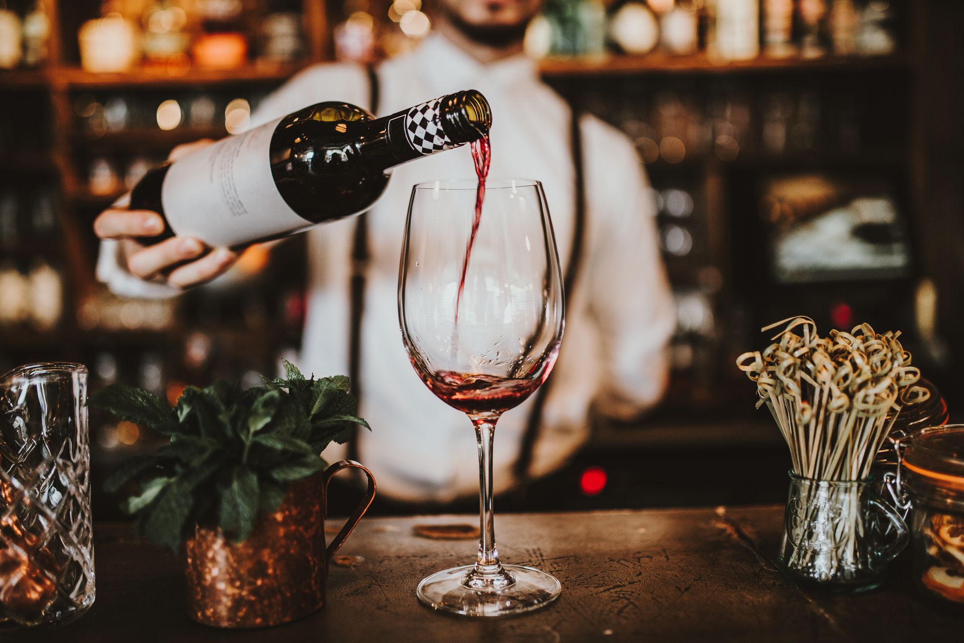 Bartender pouring red wine into a glass at a dimly lit bar counter