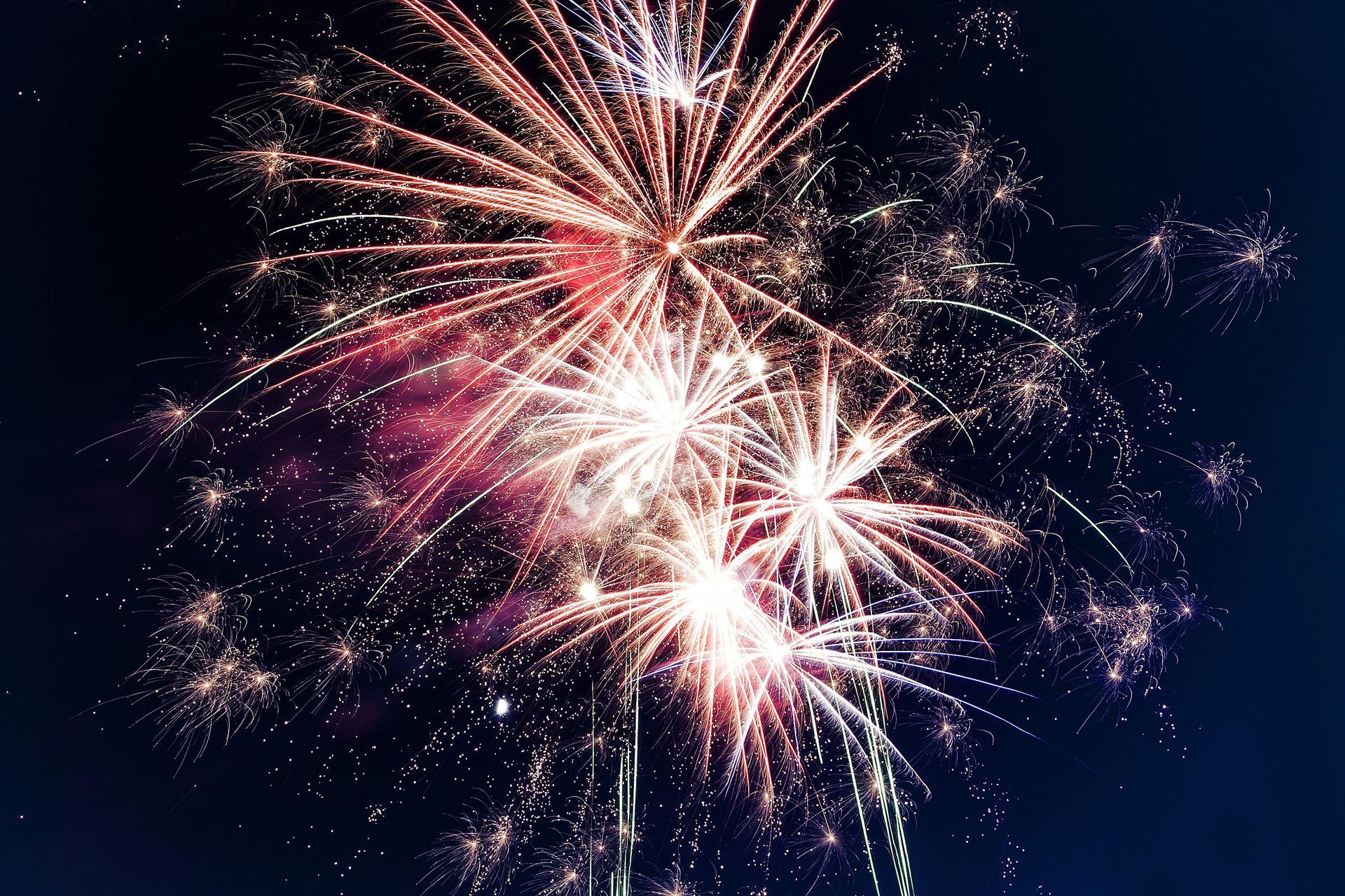 Bright, multicolored fireworks explode against a dark night sky, creating light streaks and scattered sparks.