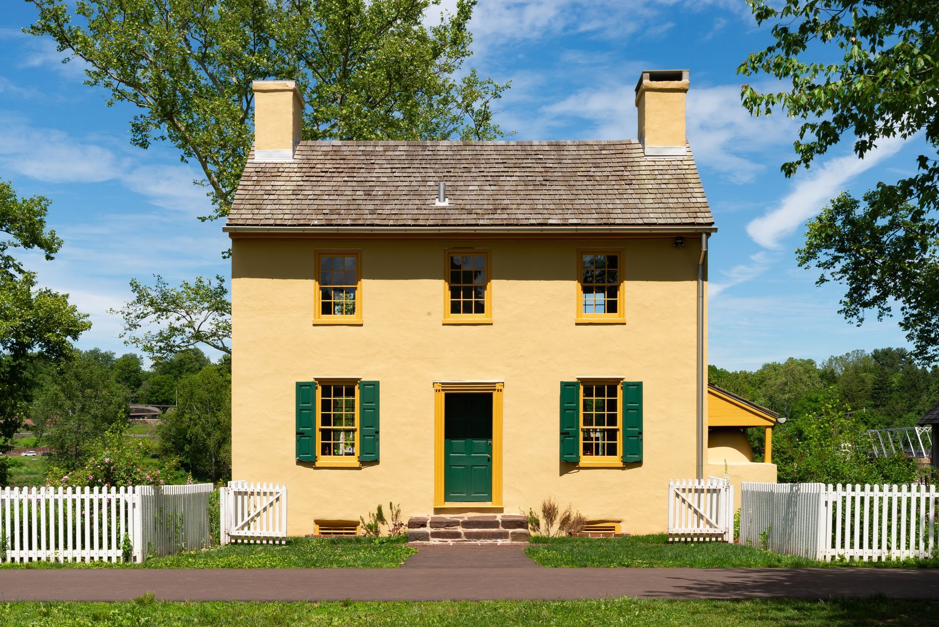 Yellow house with green shutters and white picket fence under a blue sky