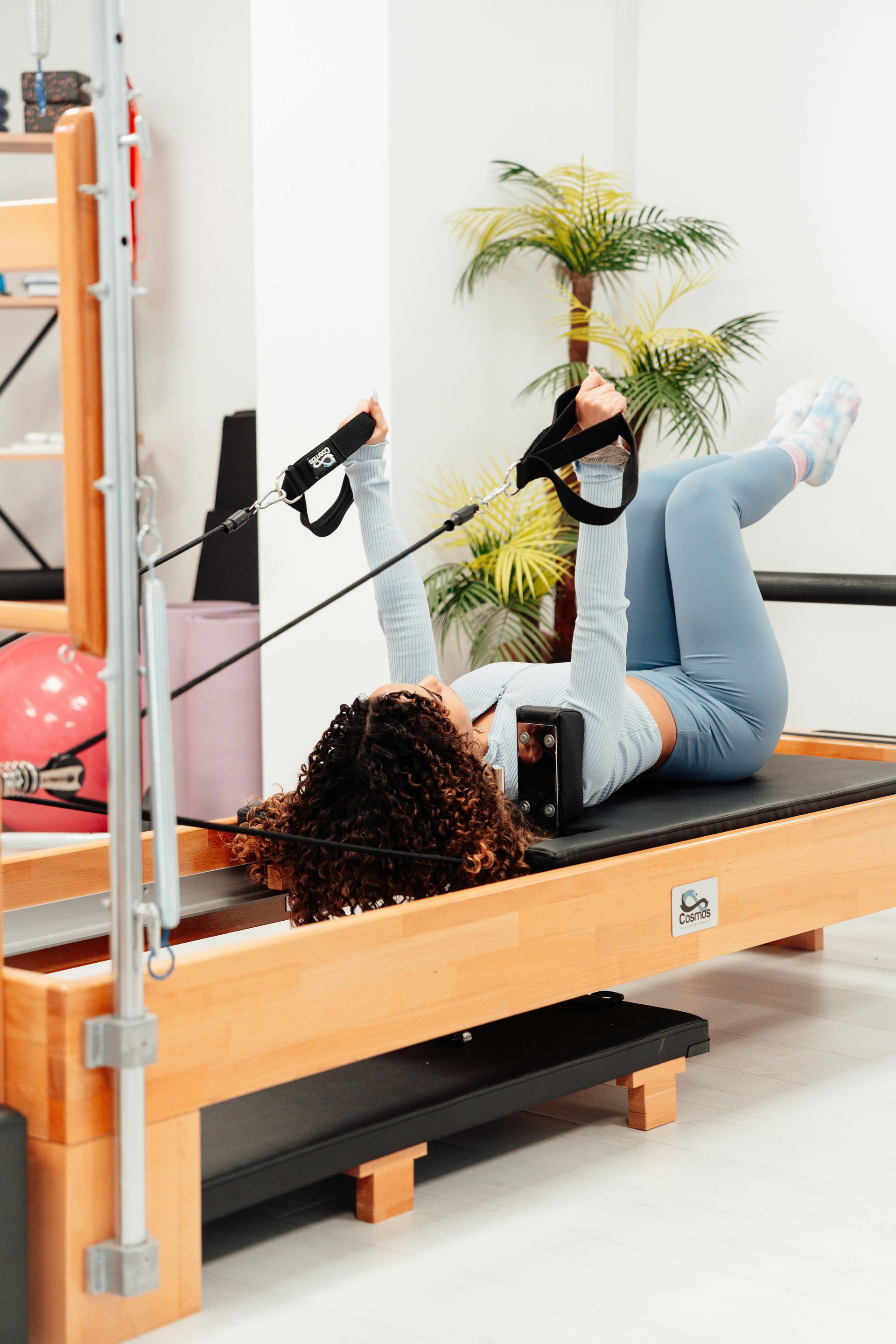 Person exercising on a Pilates reformer machine in a bright studio