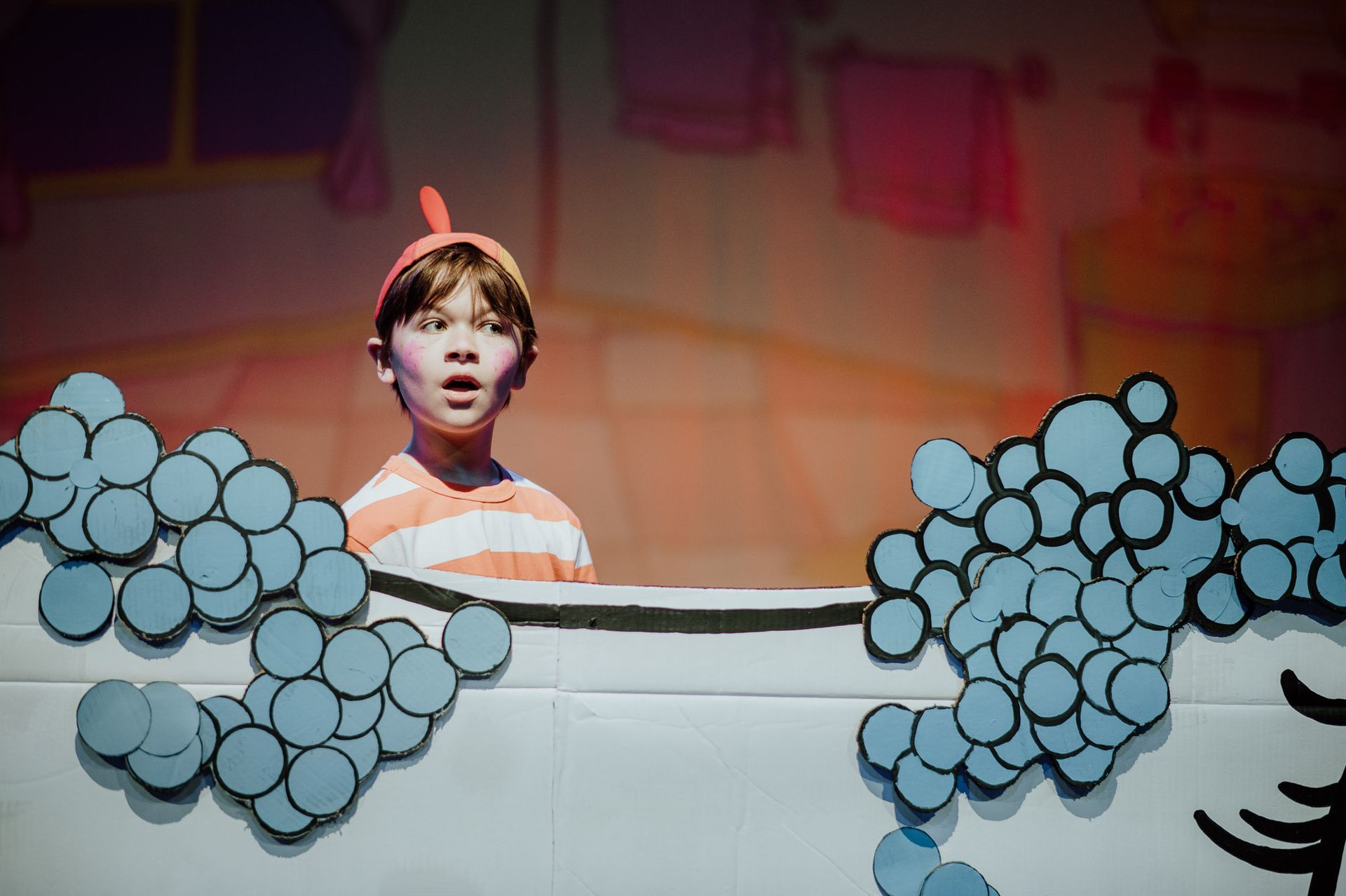 Boy in bathtub on stage, surprised expression, with paper bubbles and cartoon bathroom backdrop.