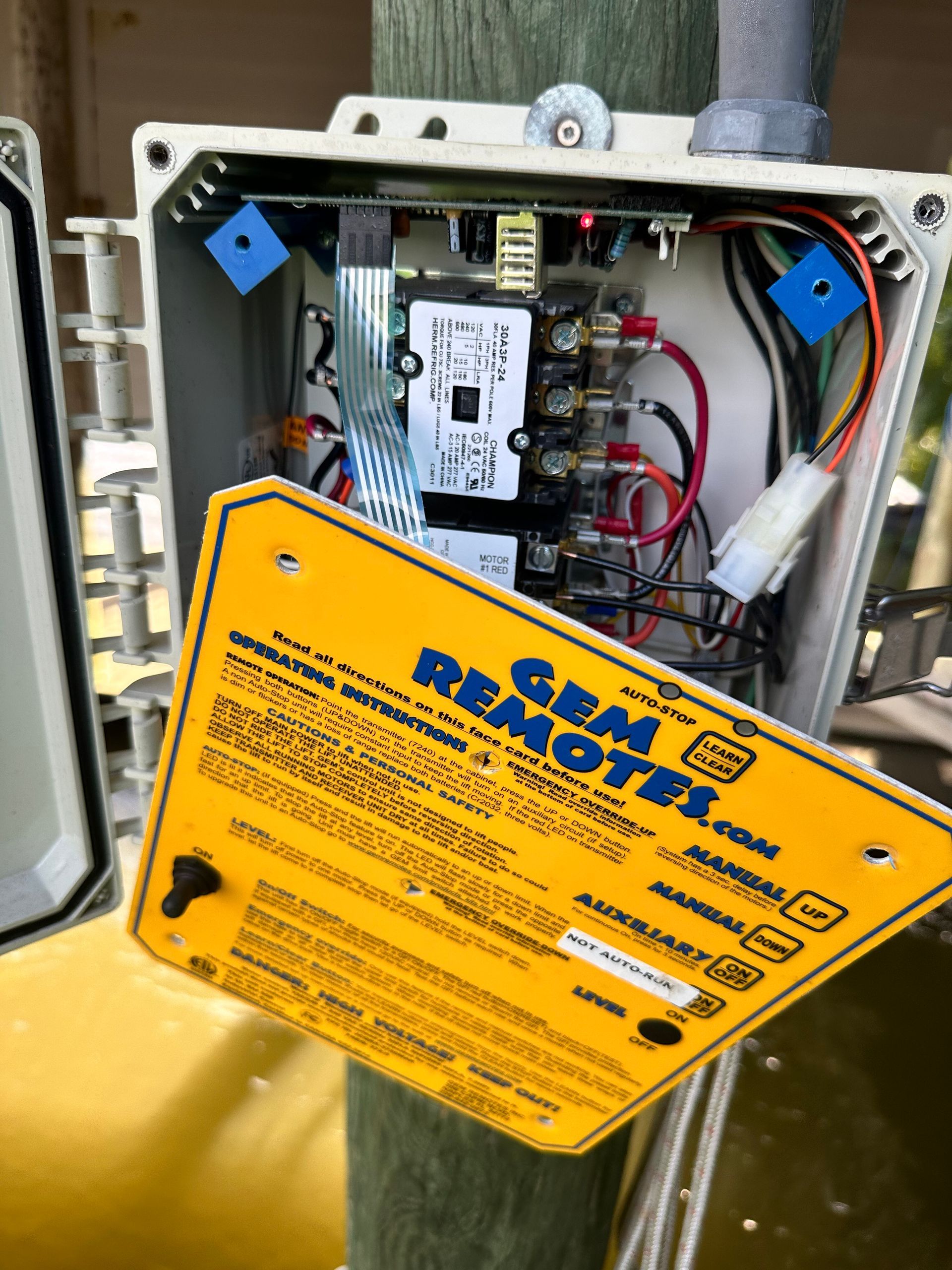 Open electrical box with wiring, circuit board, and a yellow warning label on a pole.