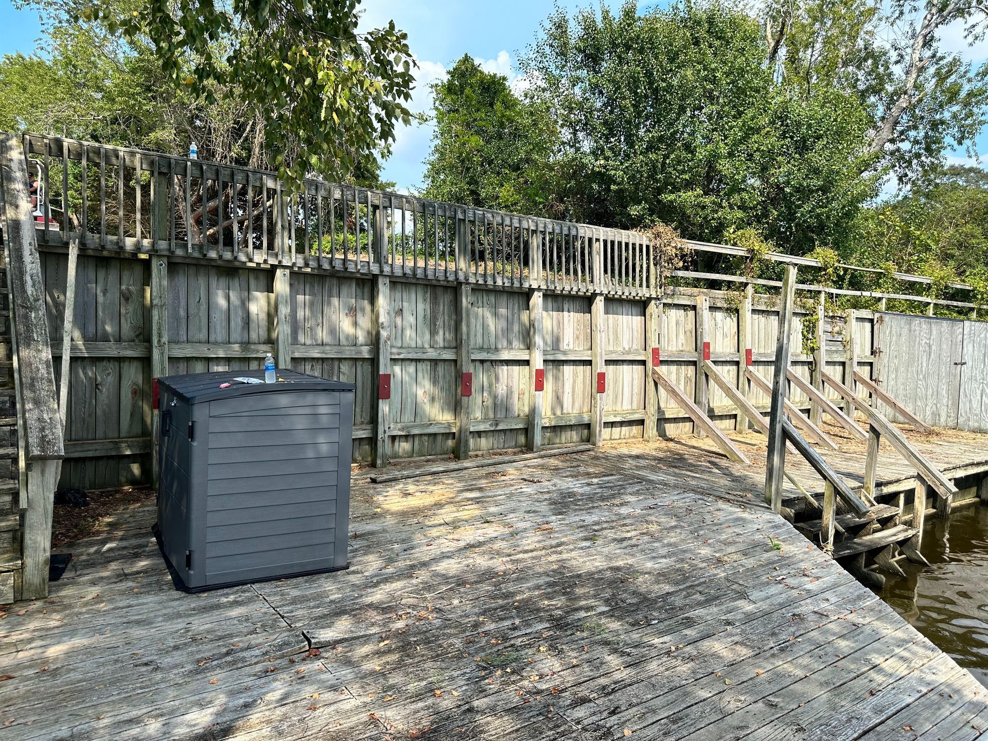 An outdoor hot tub next to a weathered wooden fence and pier on a sunny day.