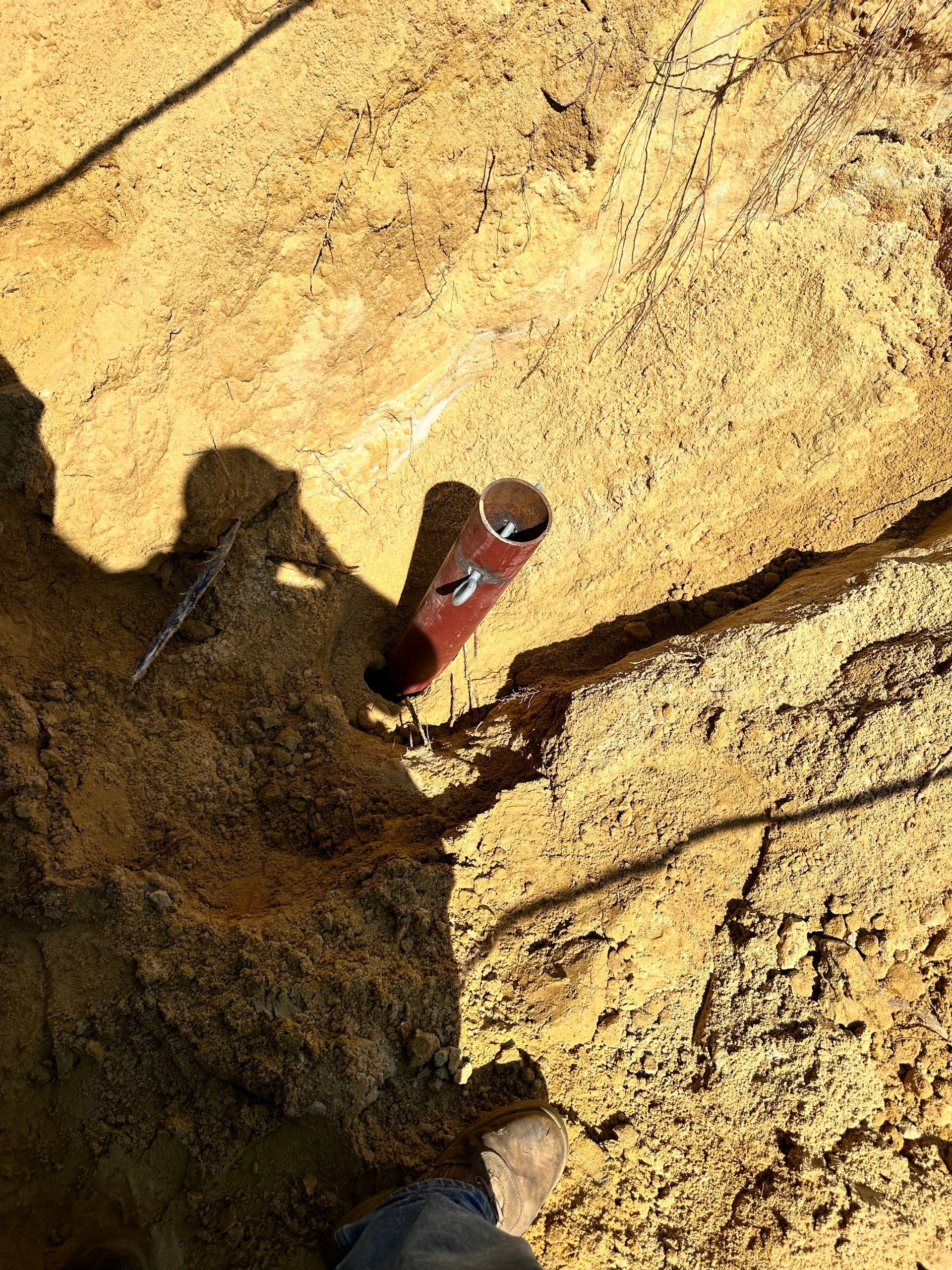 Close-up of a pipe in a sandy trench. Brown pipe, sandy brown ground, sunlight casts shadow.