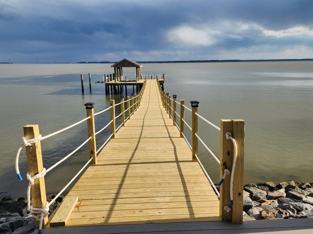 Wooden pier with rope rails leading to a small shelter over calm water under a clear sky