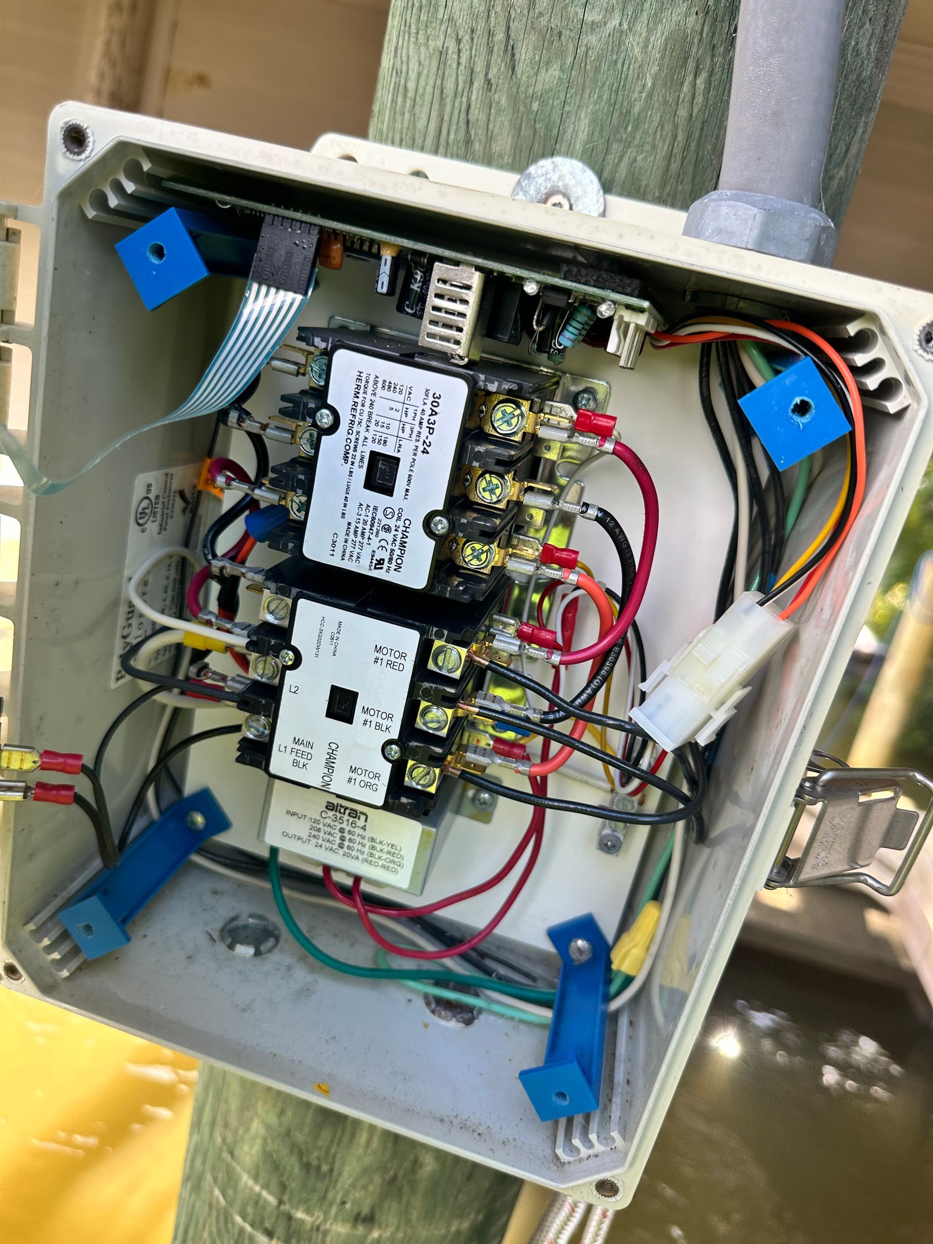 Open electrical box on a wooden post with wiring and components.