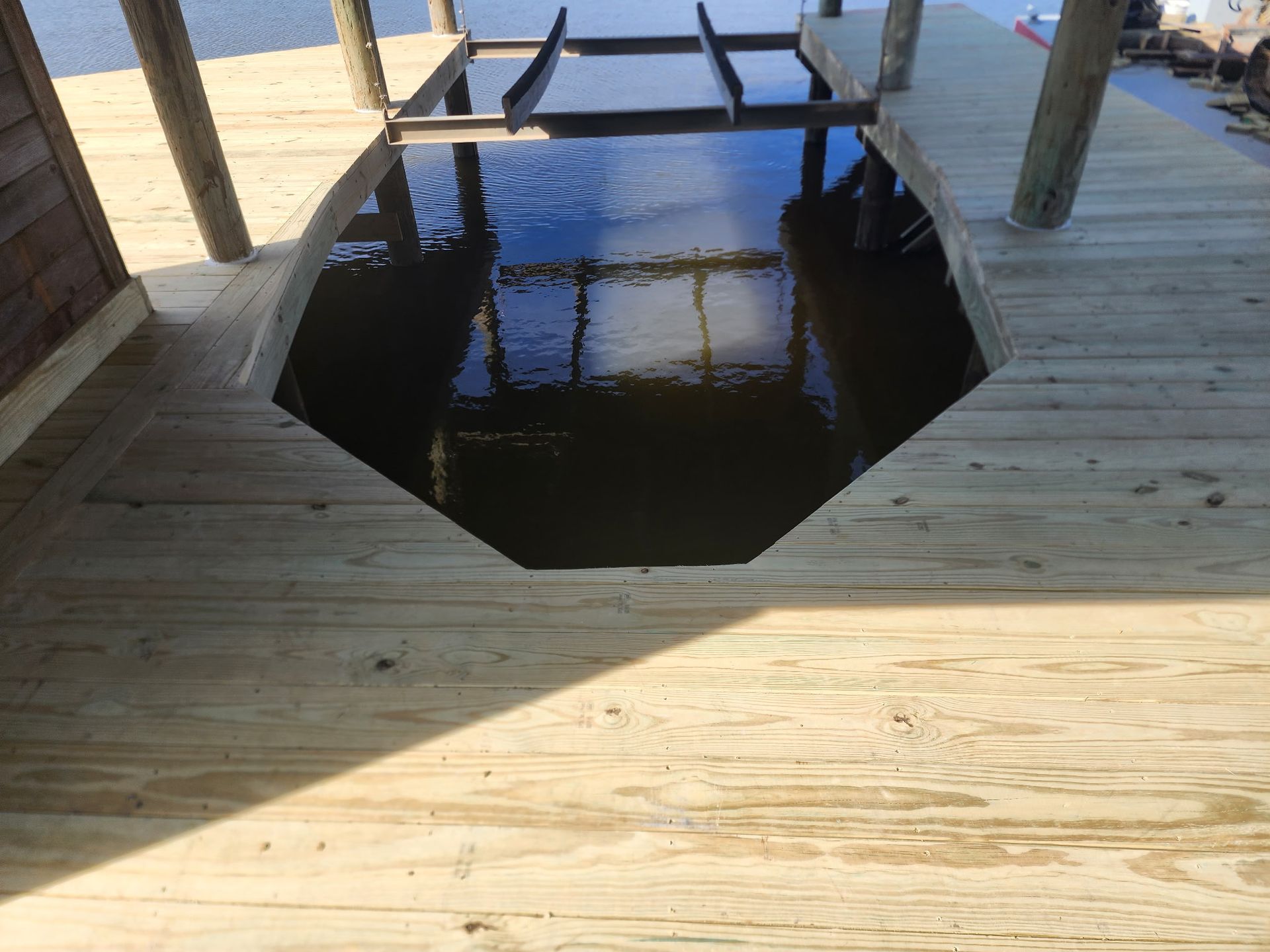 Wooden dock with an octagonal opening over dark water, reflecting a small platform and posts.
