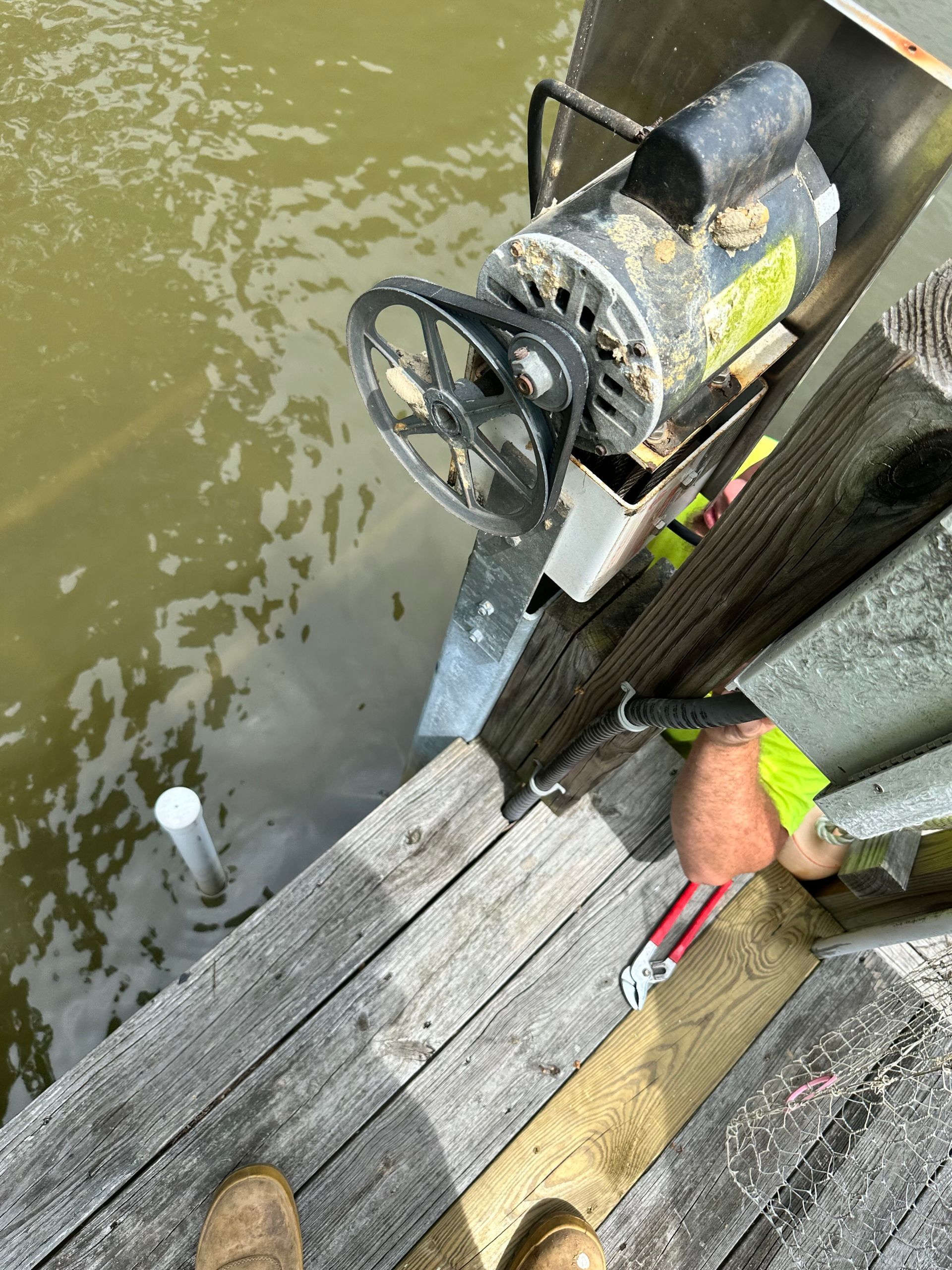 Motor on pier with pulley, in murky water.