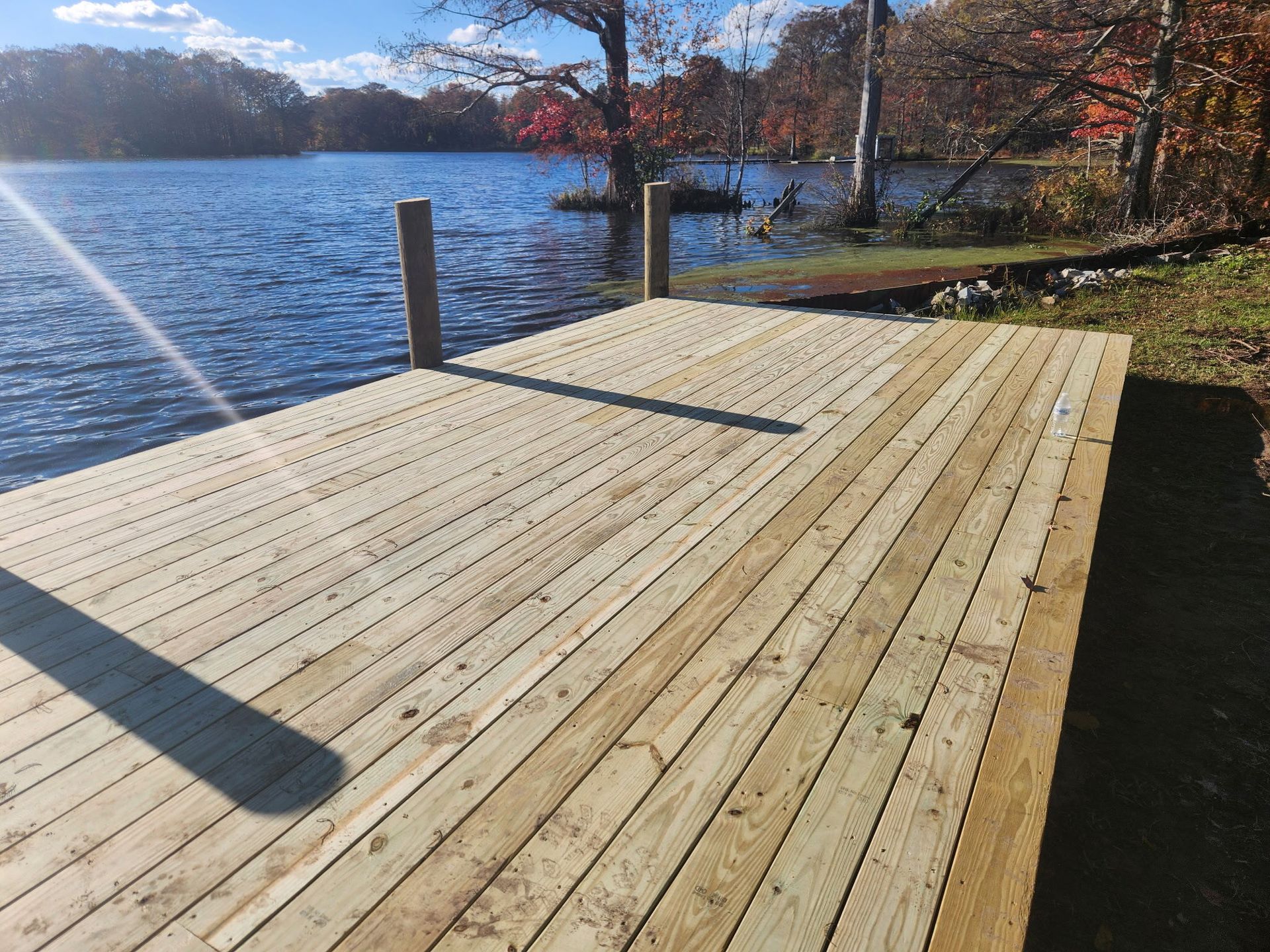 A newly constructed wooden dock overlooking a calm lake surrounded by trees during autumn.