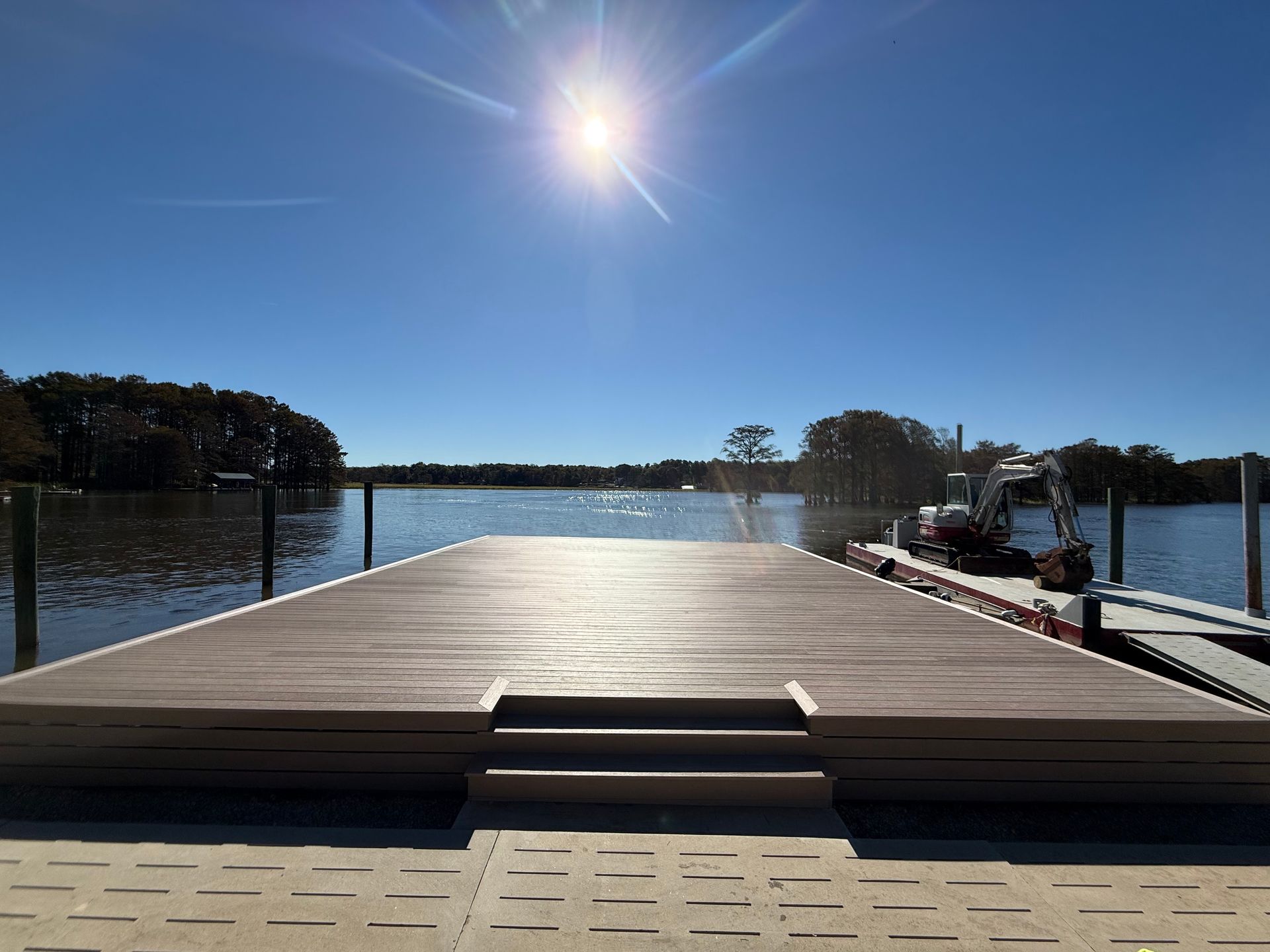 A dock on a lake under a bright sun, with steps leading down to the water.