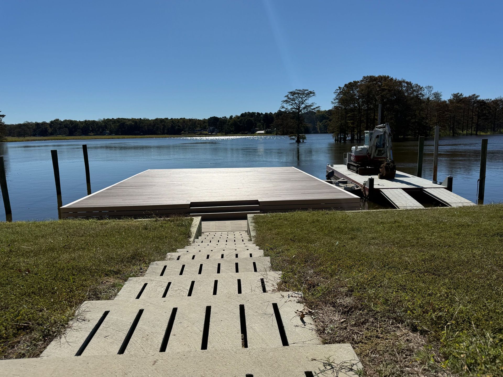 Concrete steps leading down to a dock on a lake with a blue sky.