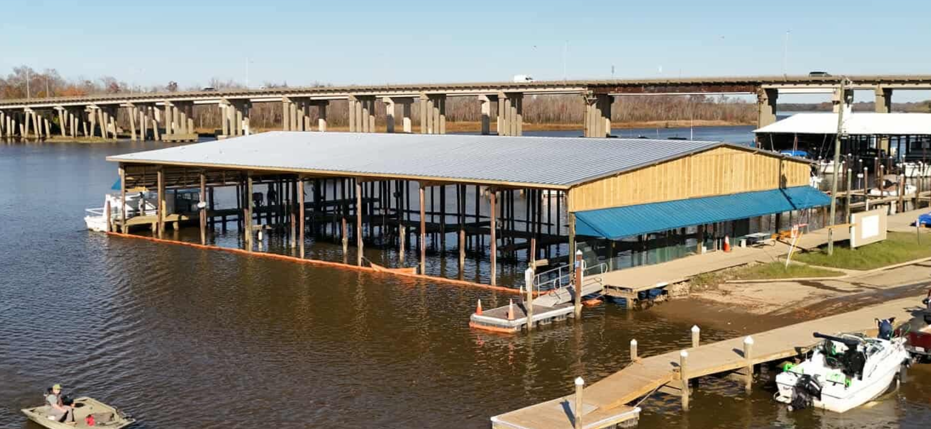 A waterfront restaurant with boats and docks, a bridge in the background, set on a river.