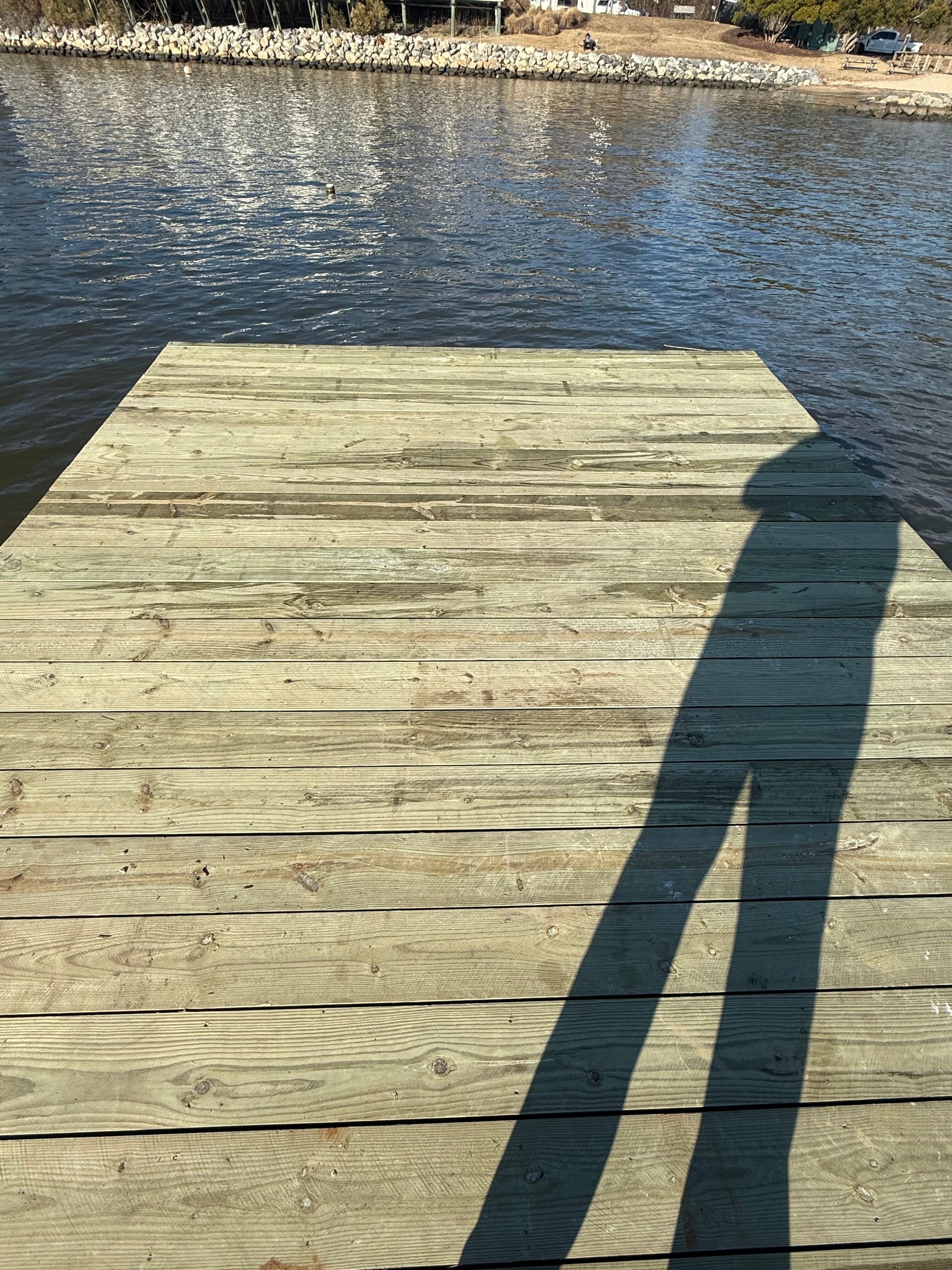 Wooden dock with a long shadow cast on it, overlooking water.
