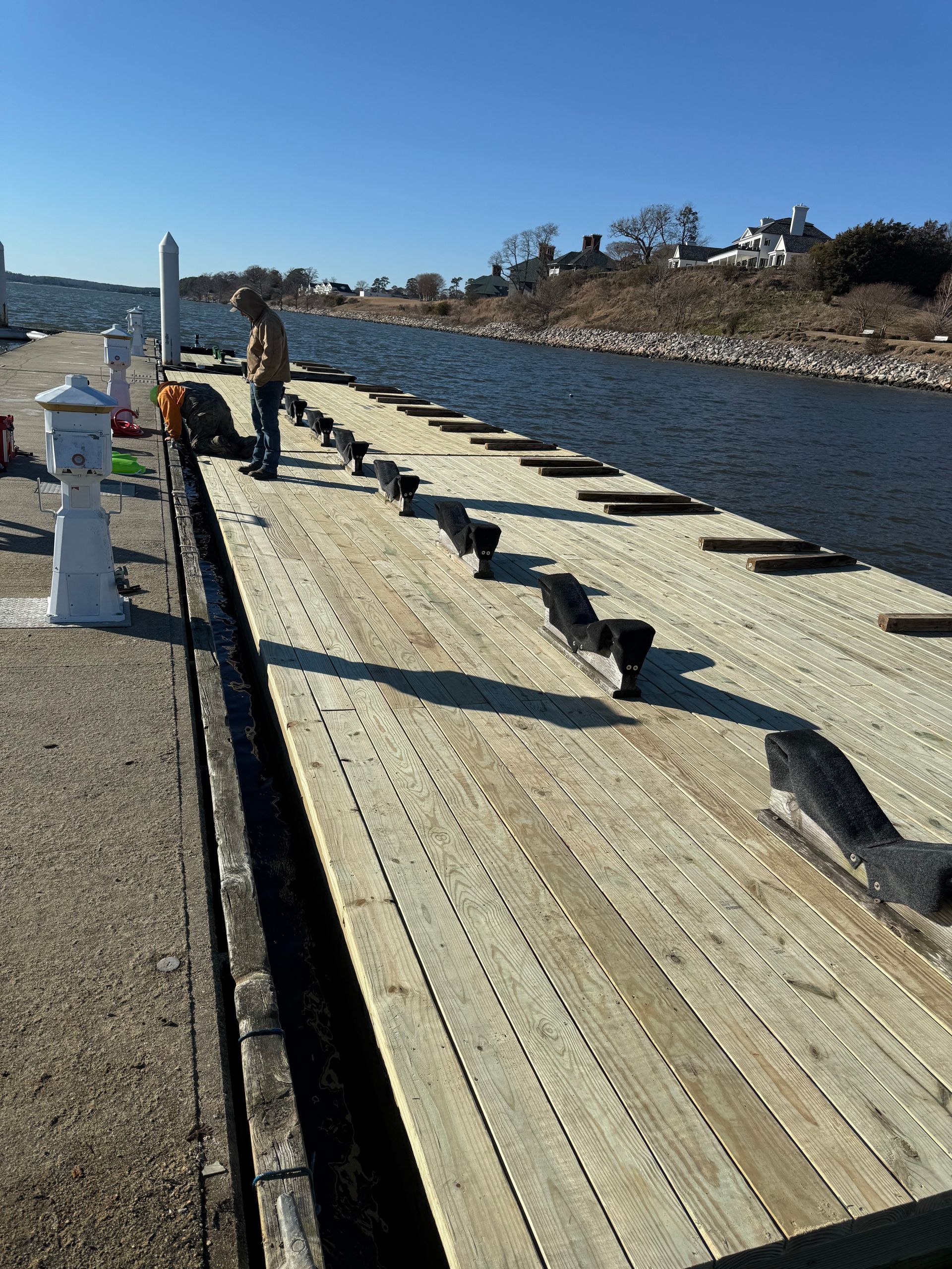 Workers on a newly planked dock. Light wood planks, water, and blue sky.