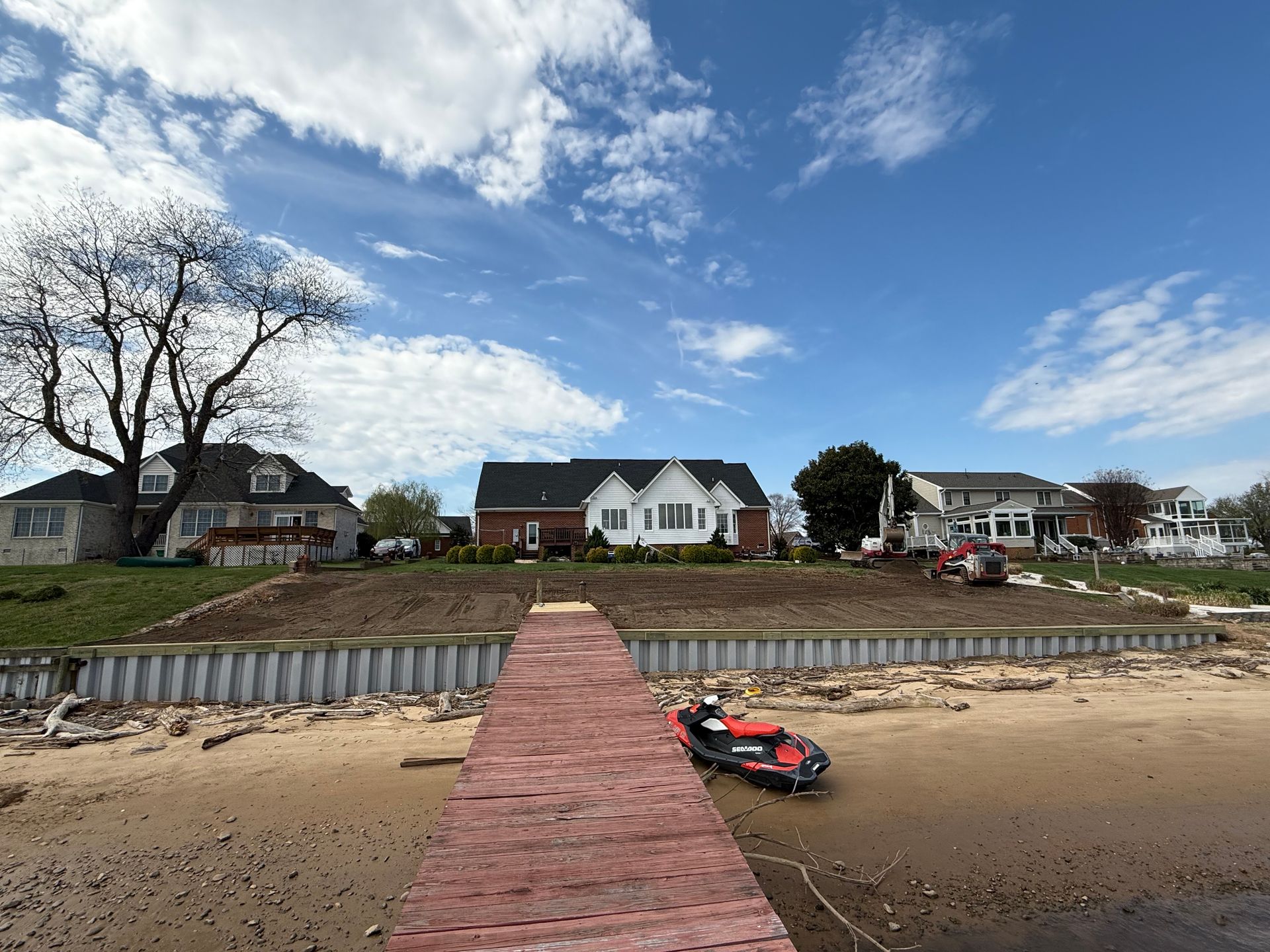 A weathered dock on a beach, houses in the background under a blue sky with clouds.