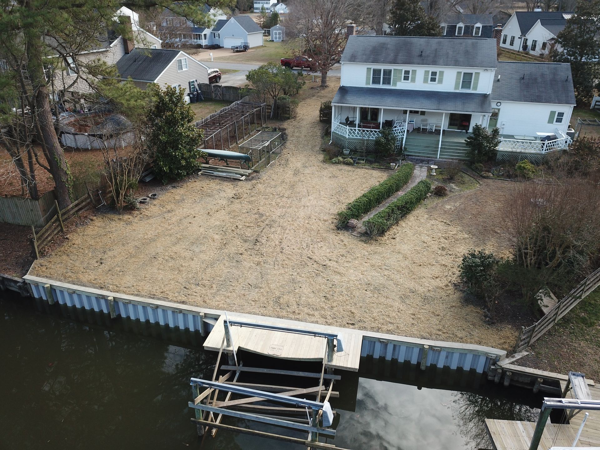 An aerial view of a waterfront property with a large, cleared yard, a bulkhead, and a boat lift extending into the water.