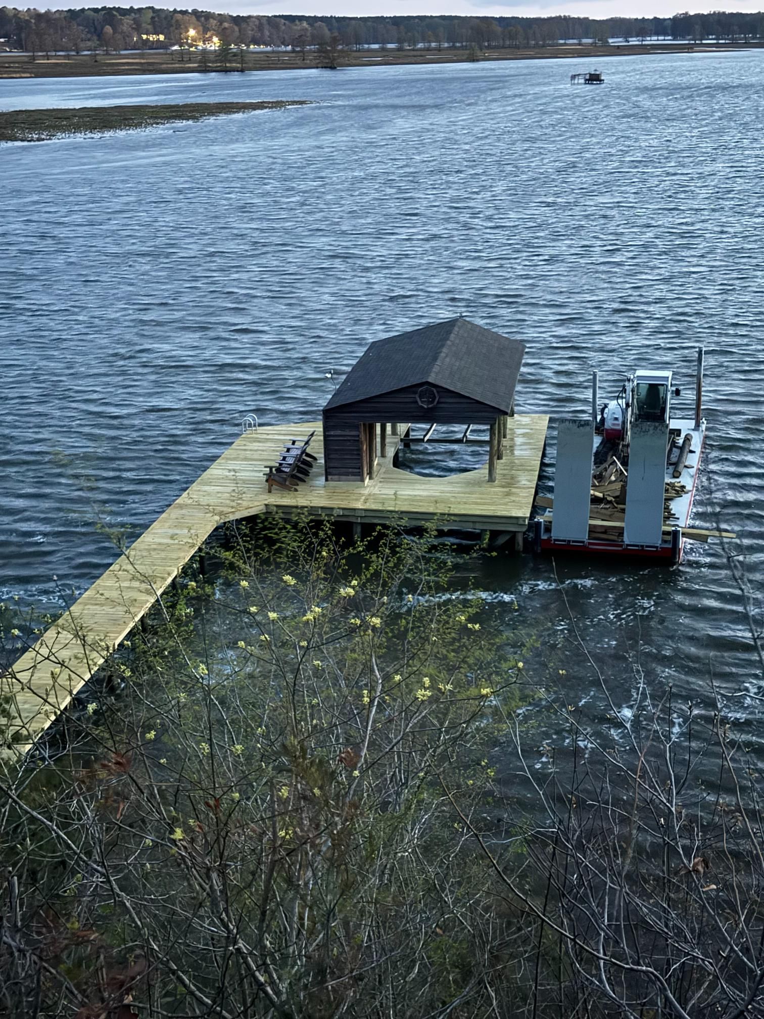 A wooden pier with a boat house extends into a lake under a cloudy sky.