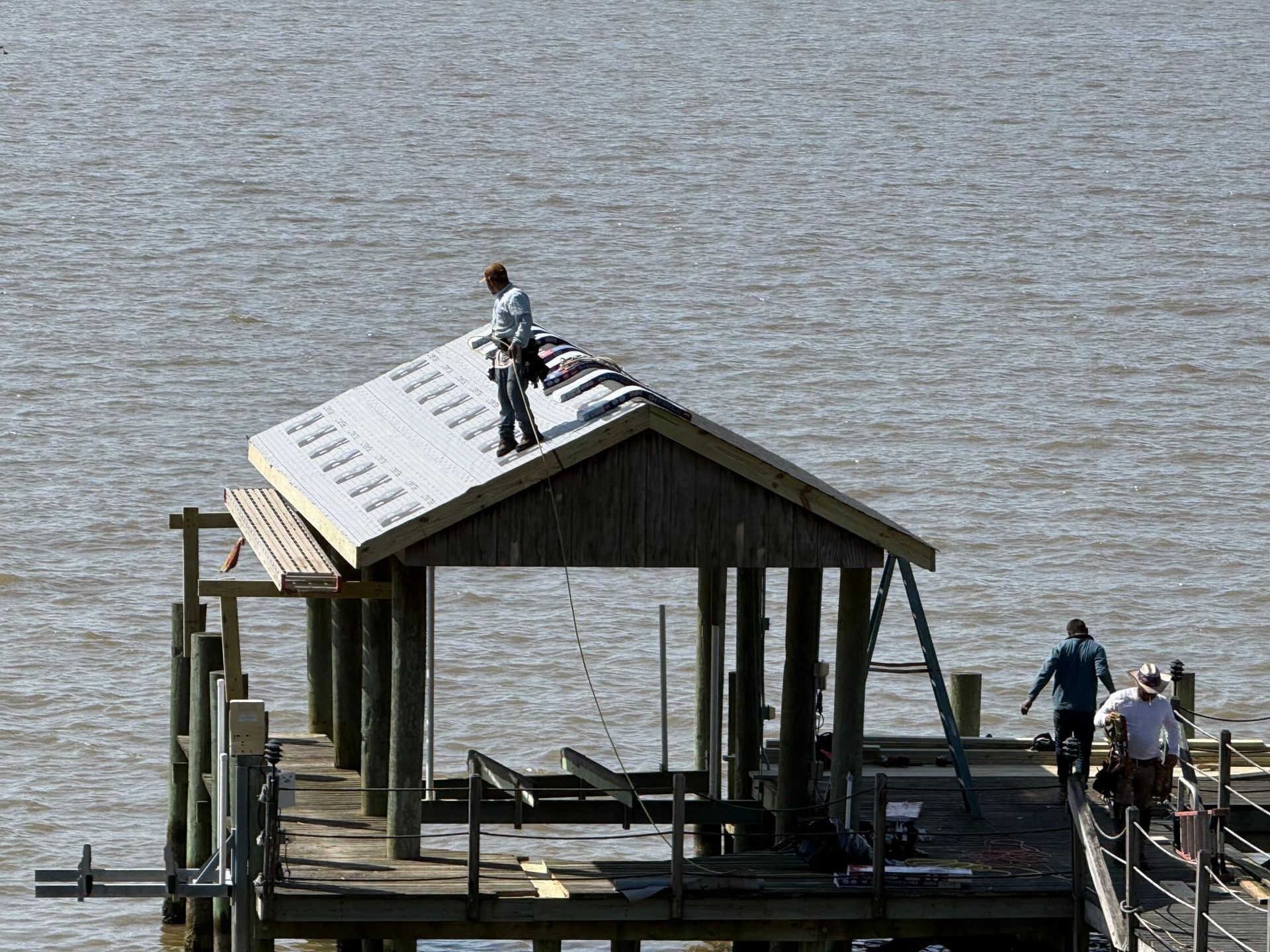 Person standing on a small wooden dock shed by the water, with others nearby at the dock edge