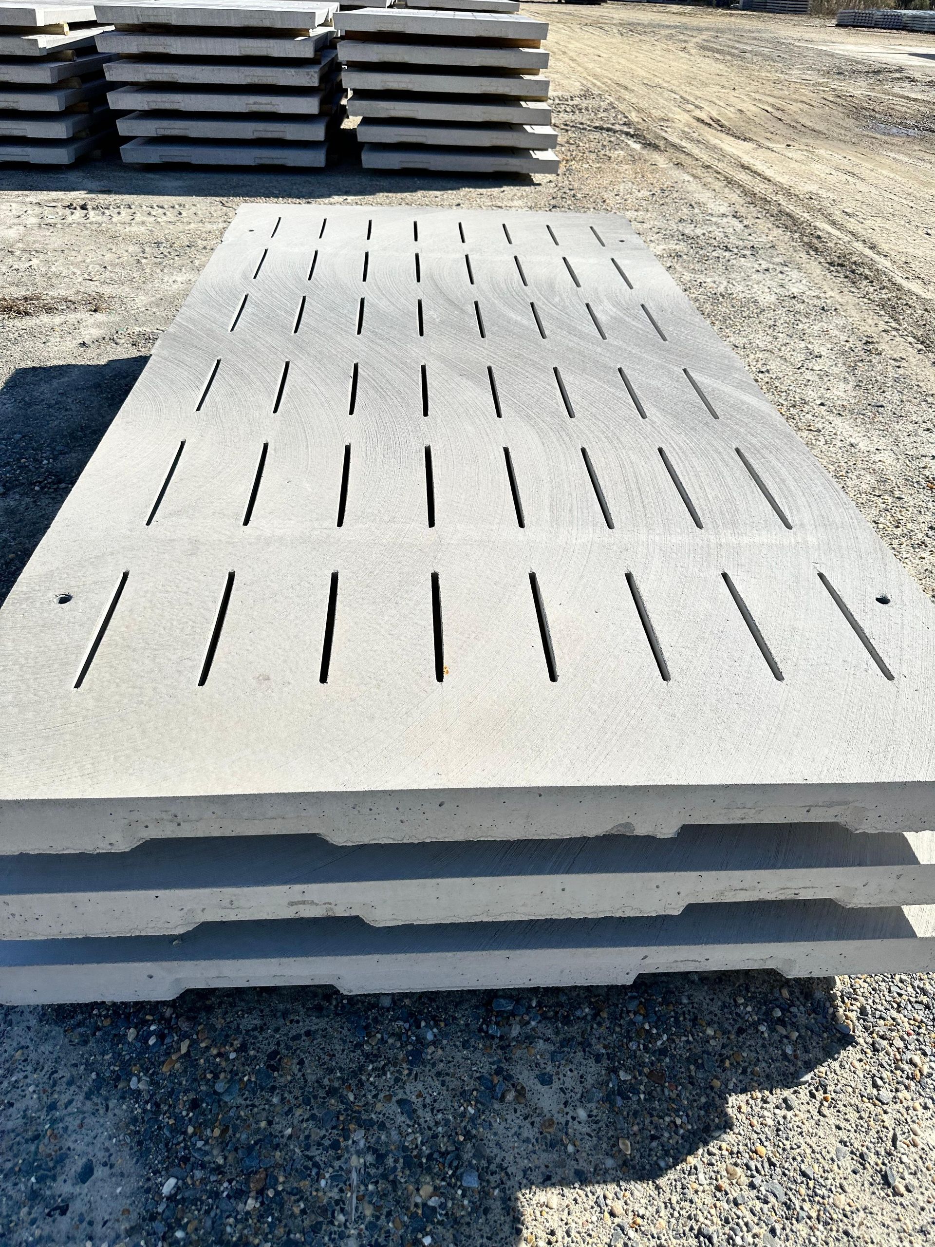Stack of gray concrete trench drain covers with slotted openings, outdoors.