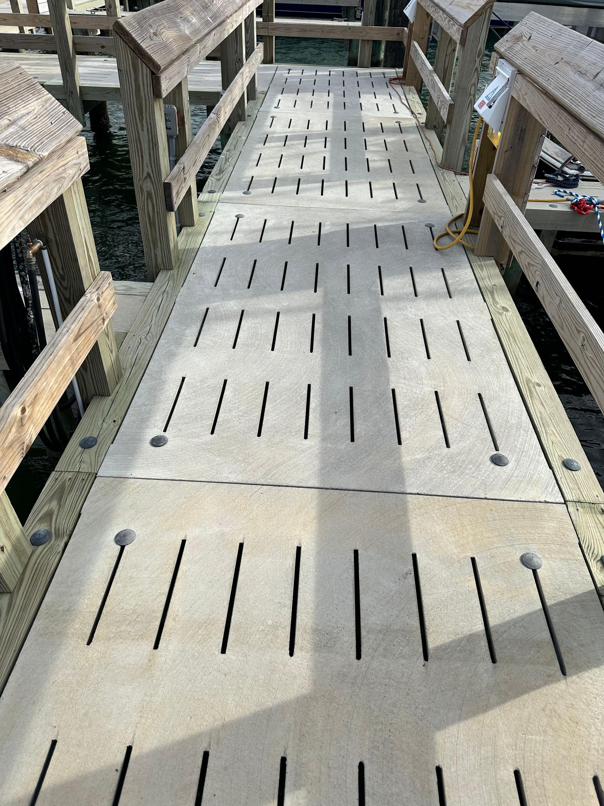 Wooden pier walkway with slotted, light-colored decking, and wooden railings.
